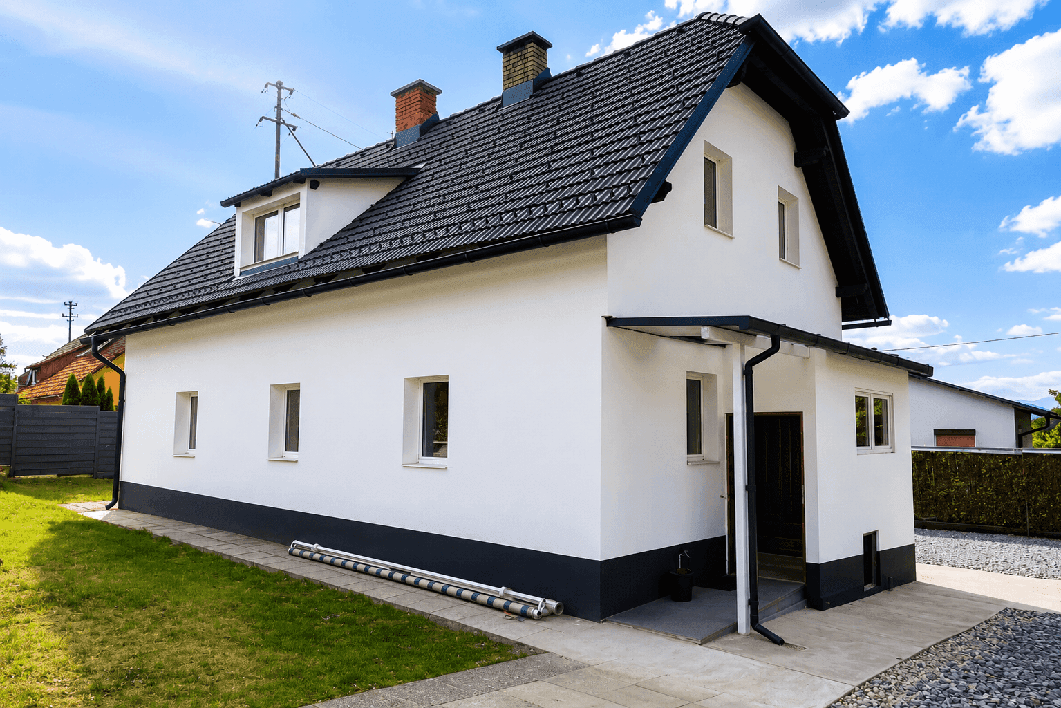 Freistehendes Einfamilienhaus mit weißer Fassade, dunklem Ziegeldach und einem kleinen Vorgarten.