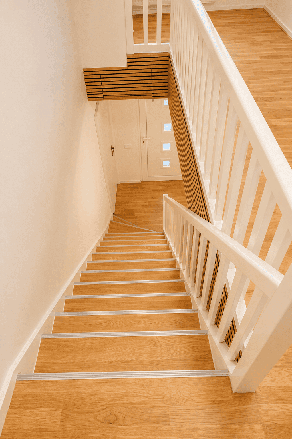Treppenhaus mit Holzstufen und weißem Geländer, das in das Erdgeschoss führt.