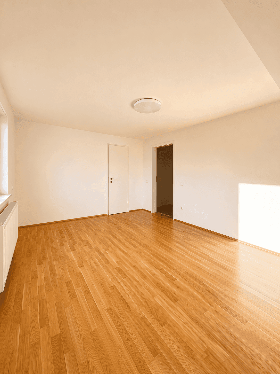 Geräumiges Zimmer mit Parkettboden, weißen Wänden und viel natürlichem Licht.