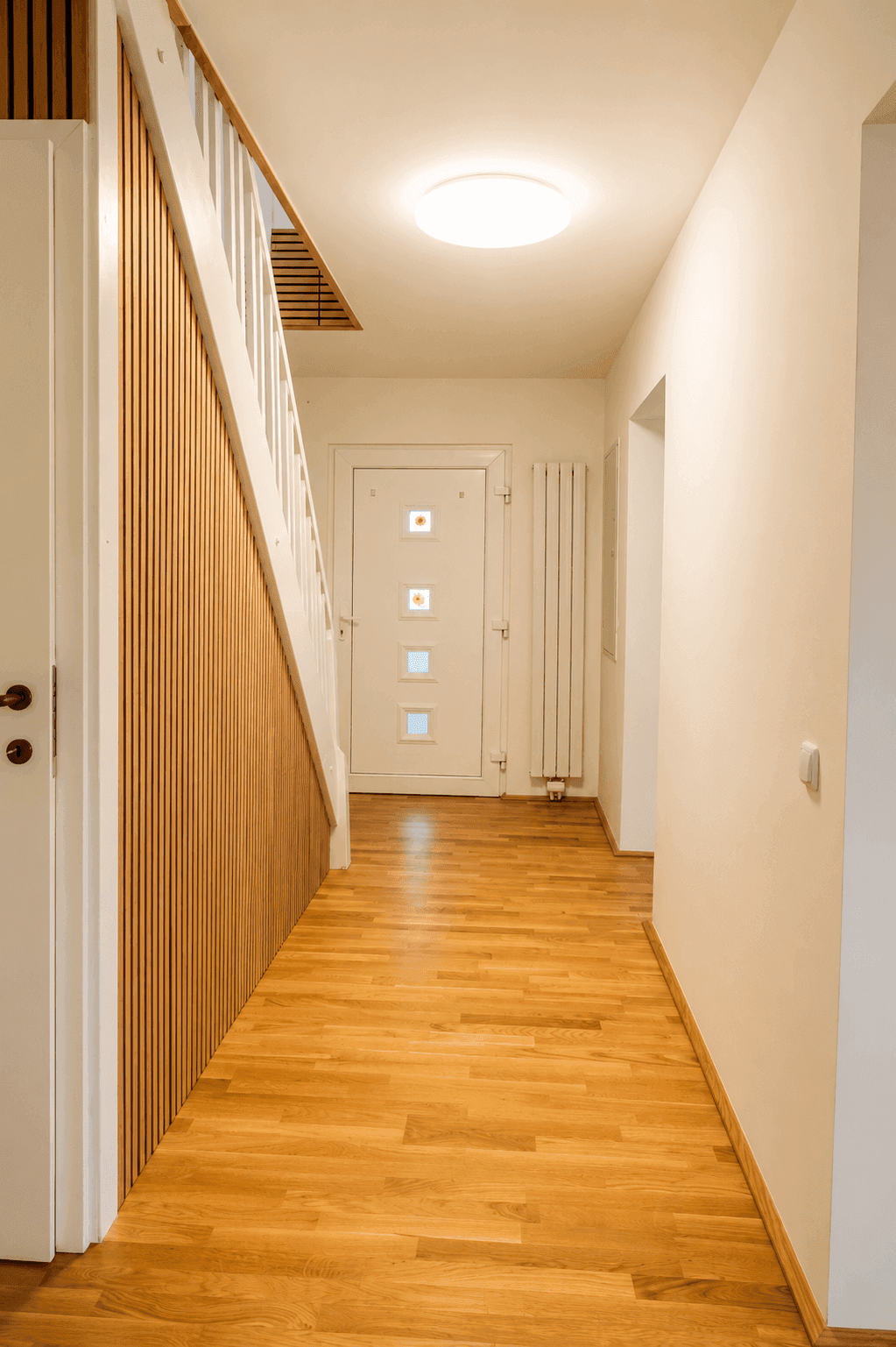 Geräumiger Flur mit Holzparkettboden, weißer Treppe und einer modernen Eingangstür.