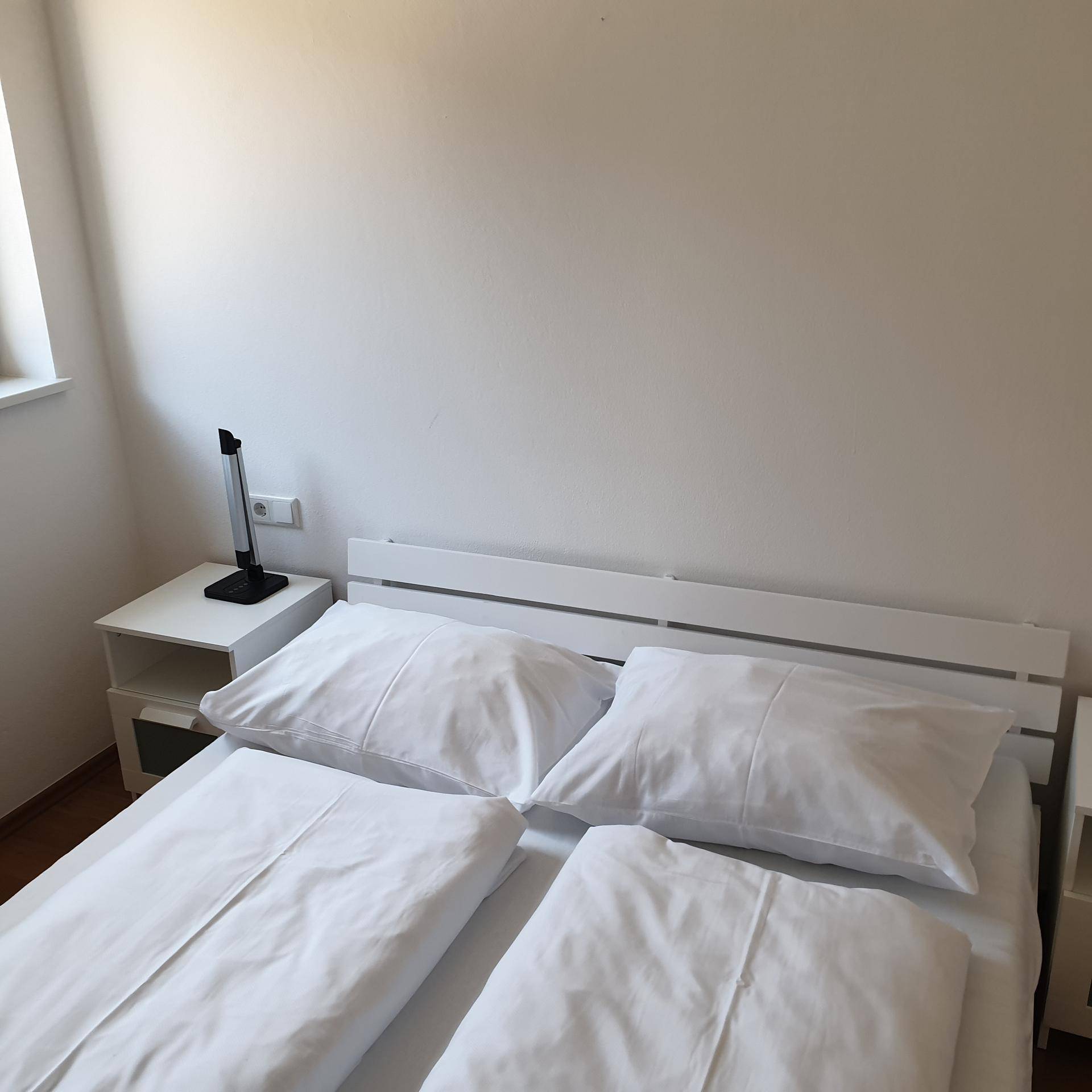 Helles Schlafzimmer mit Doppelbett, Nachttischen und weißer Bettwäsche.