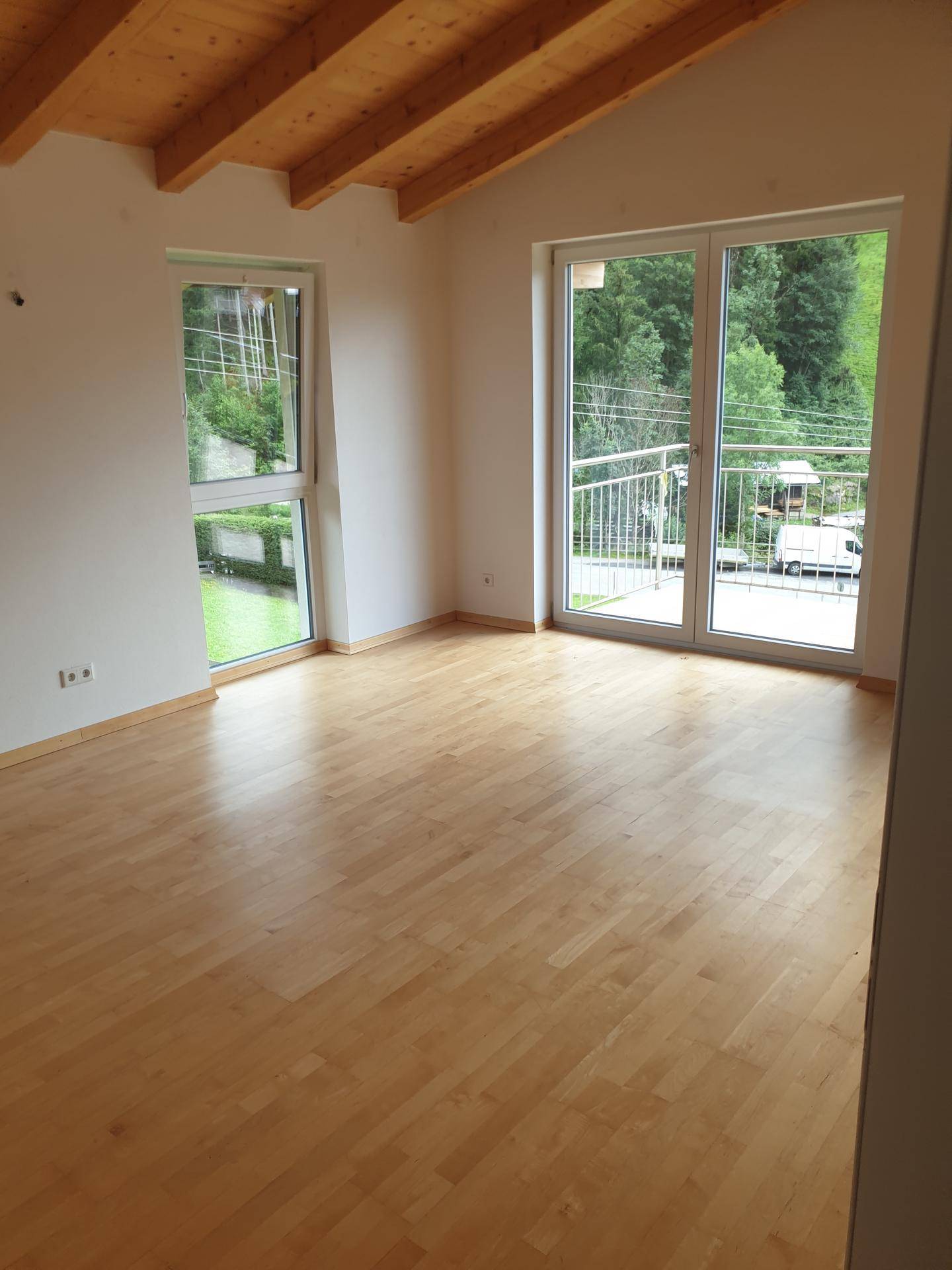 Geräumiges Zimmer mit Holzbalkendecke, Parkettboden und Balkonzugang mit grüner Aussicht.