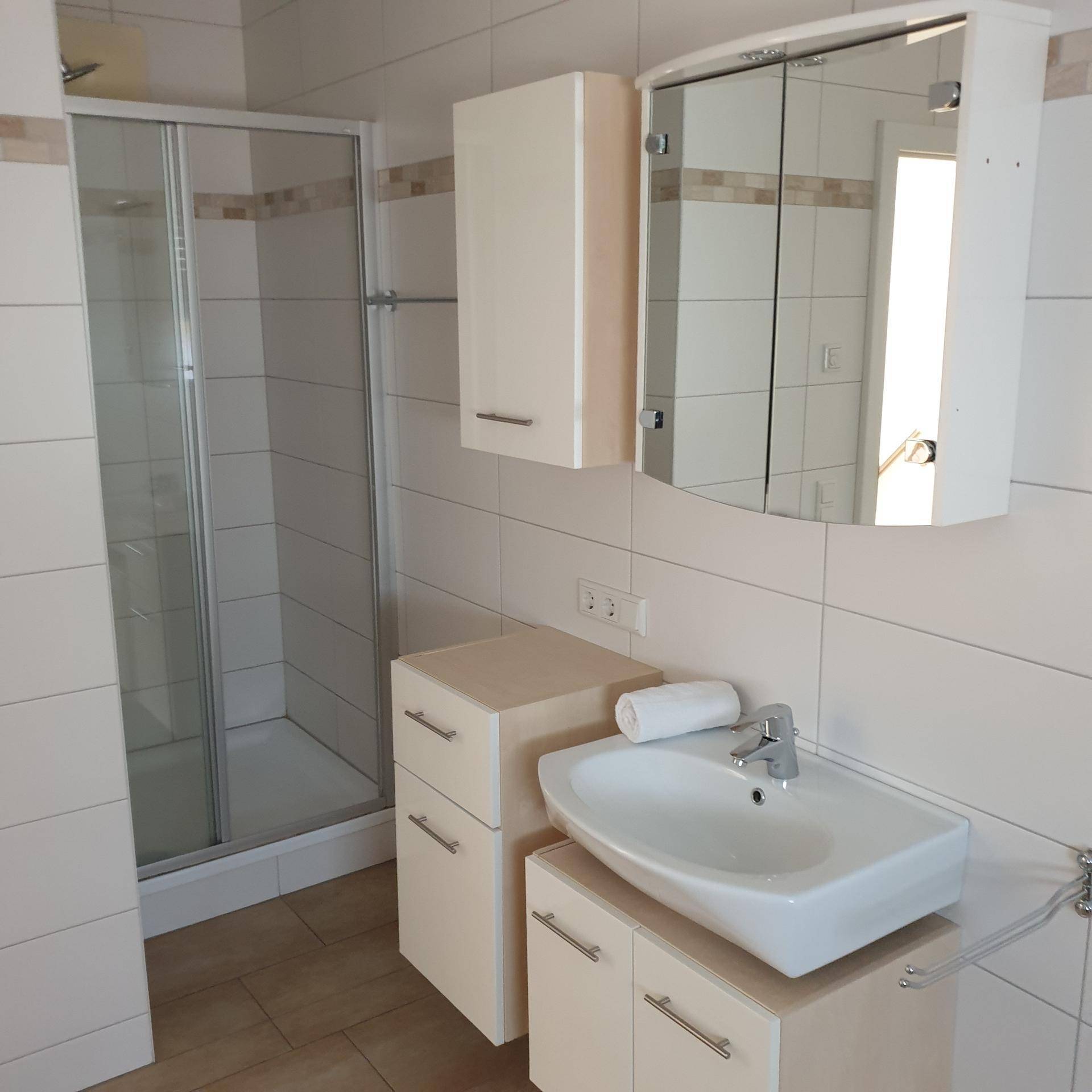 Modernes Badezimmer mit Duschkabine, Waschbecken und hellen Fliesen.