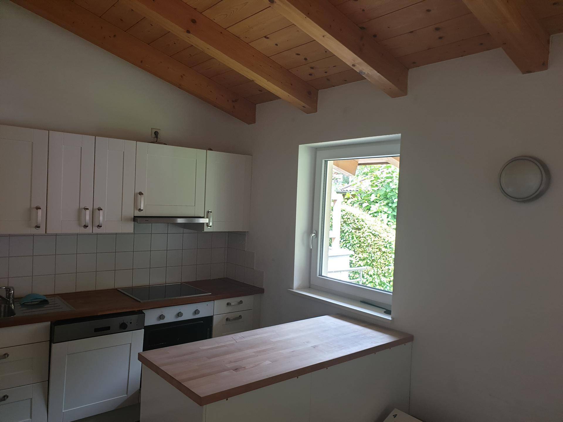 Kleine Küche mit weißen Schränken, Holzarbeitsplatte und Holzbalkendecke.