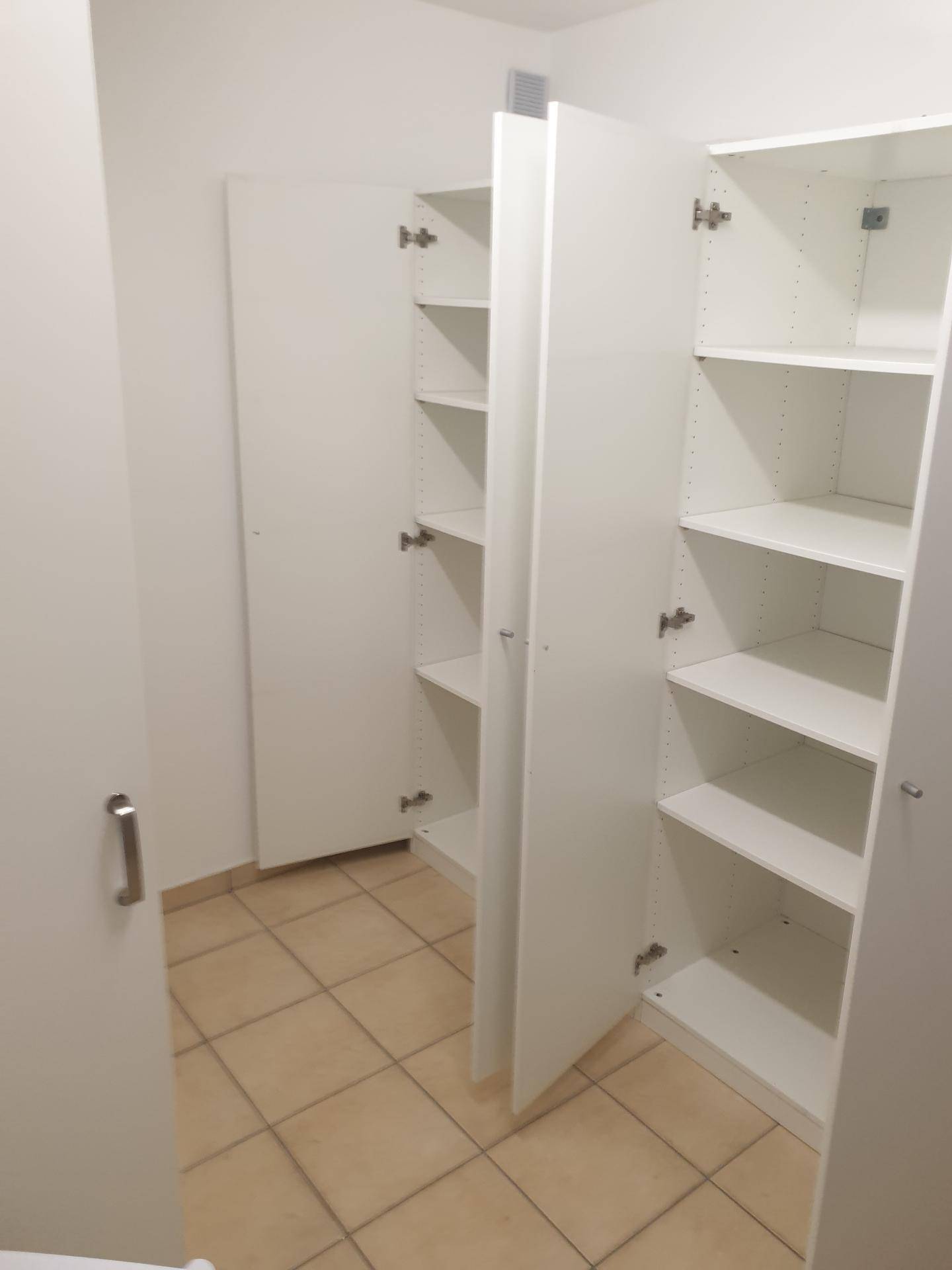 Praktischer Abstellraum mit weißen Einbauschränken und Fliesenboden.
