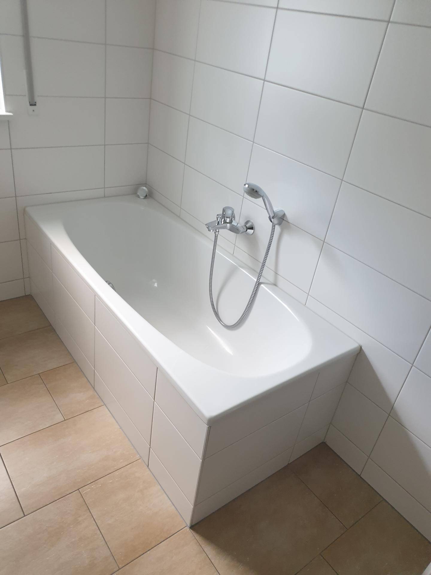 Eingebaute Badewanne mit Duscharmatur und weißen Fliesen.