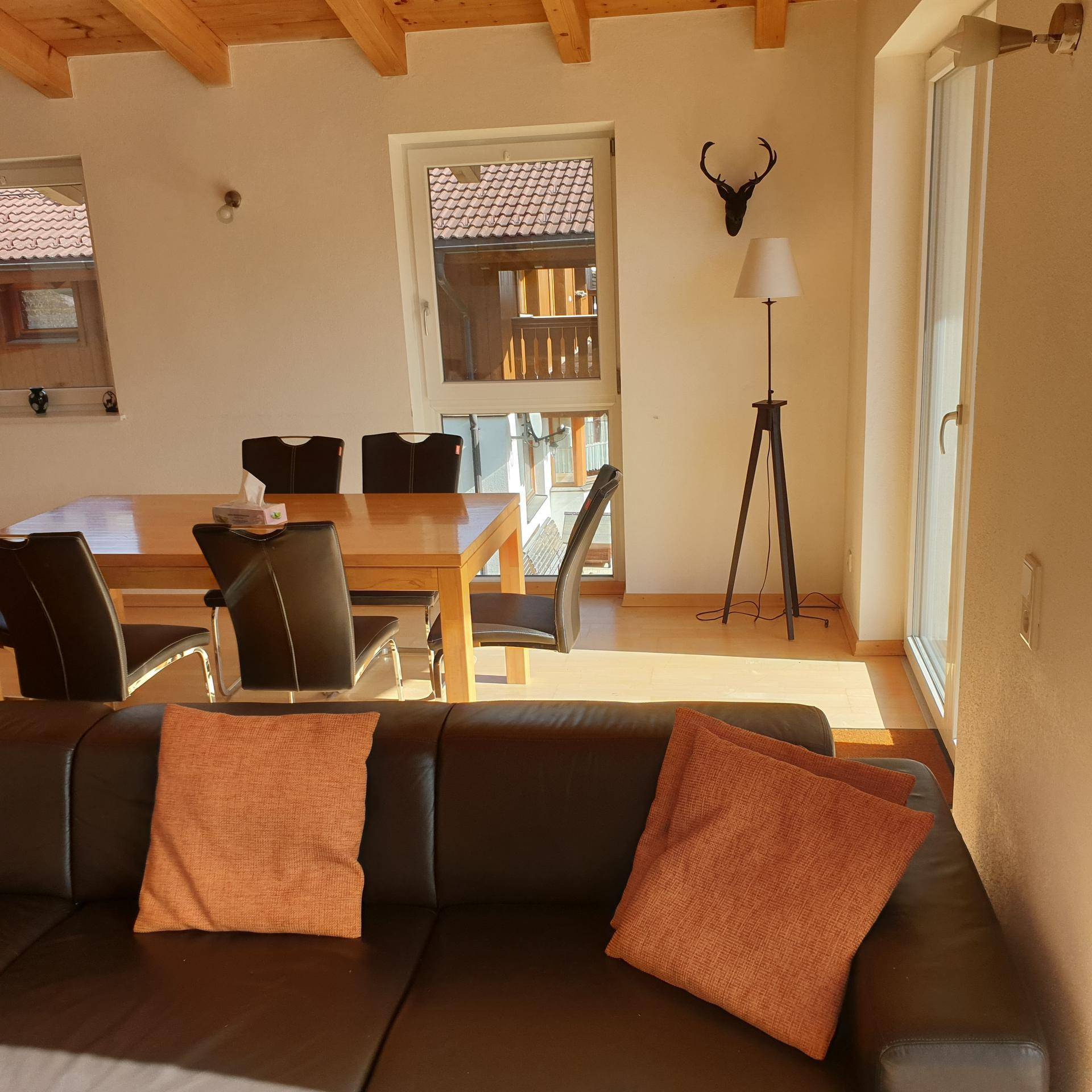 Lichtdurchfluteter Wohn- und Essbereich mit Holzbalken an der Decke und Zugang zum Balkon.