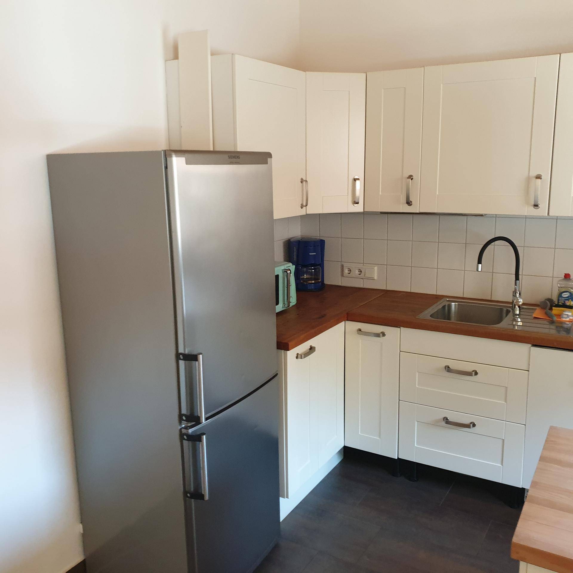 Funktionale Küche mit weißen Schränken, Holz-Arbeitsplatte und großem Kühlschrank.