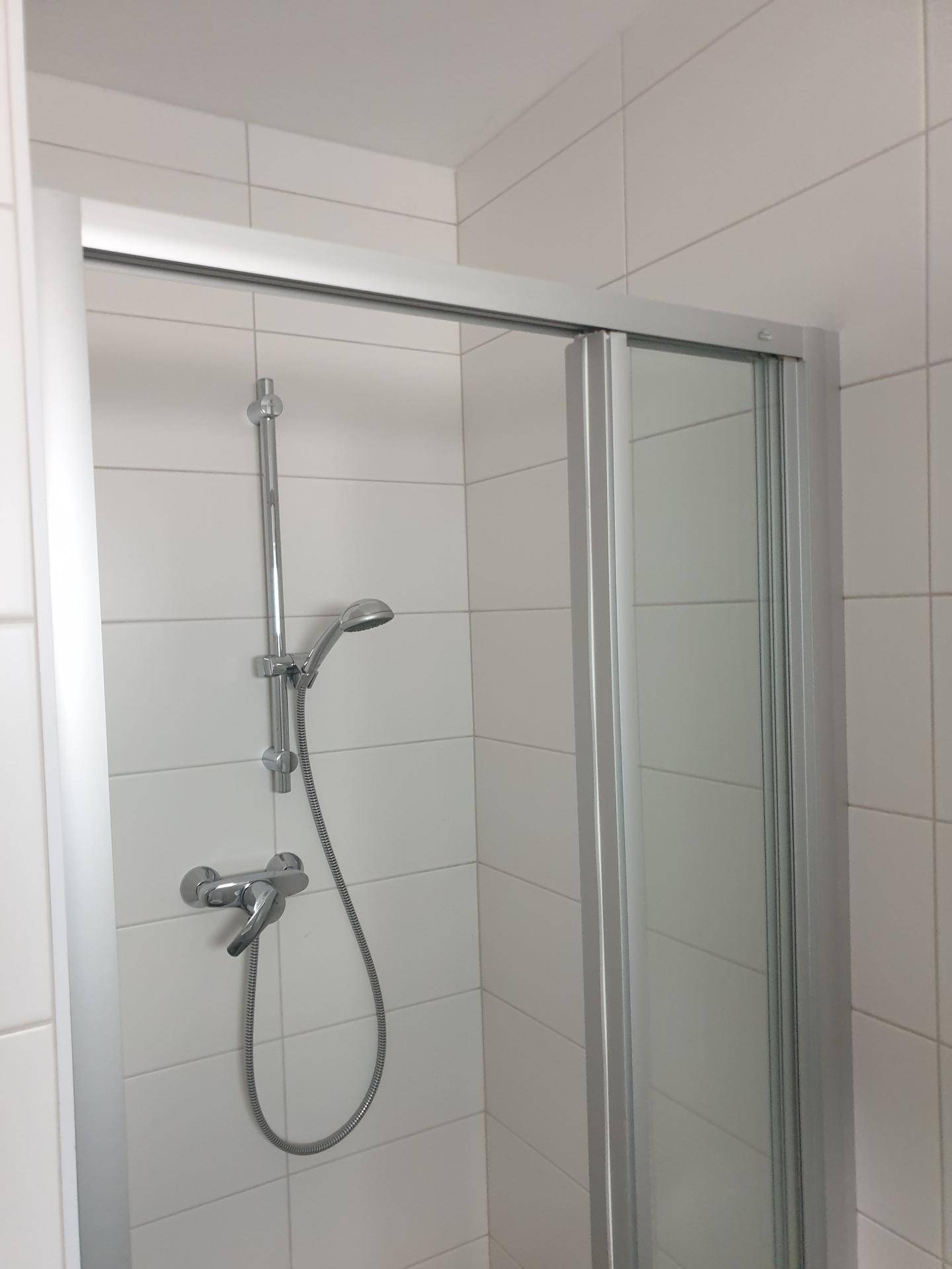 Duschkabine mit Duschkopf und weißen Wandfliesen.