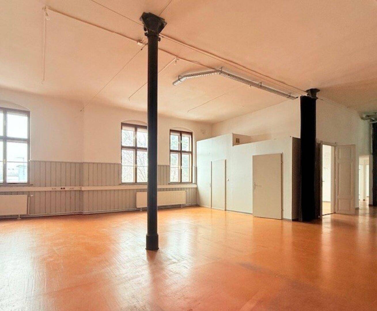 Weitläufiger Loft-Raum mit Säulen, hohen Decken und mehreren Türen, die zu weiteren Bereichen führen, bietet flexible Nutzung.