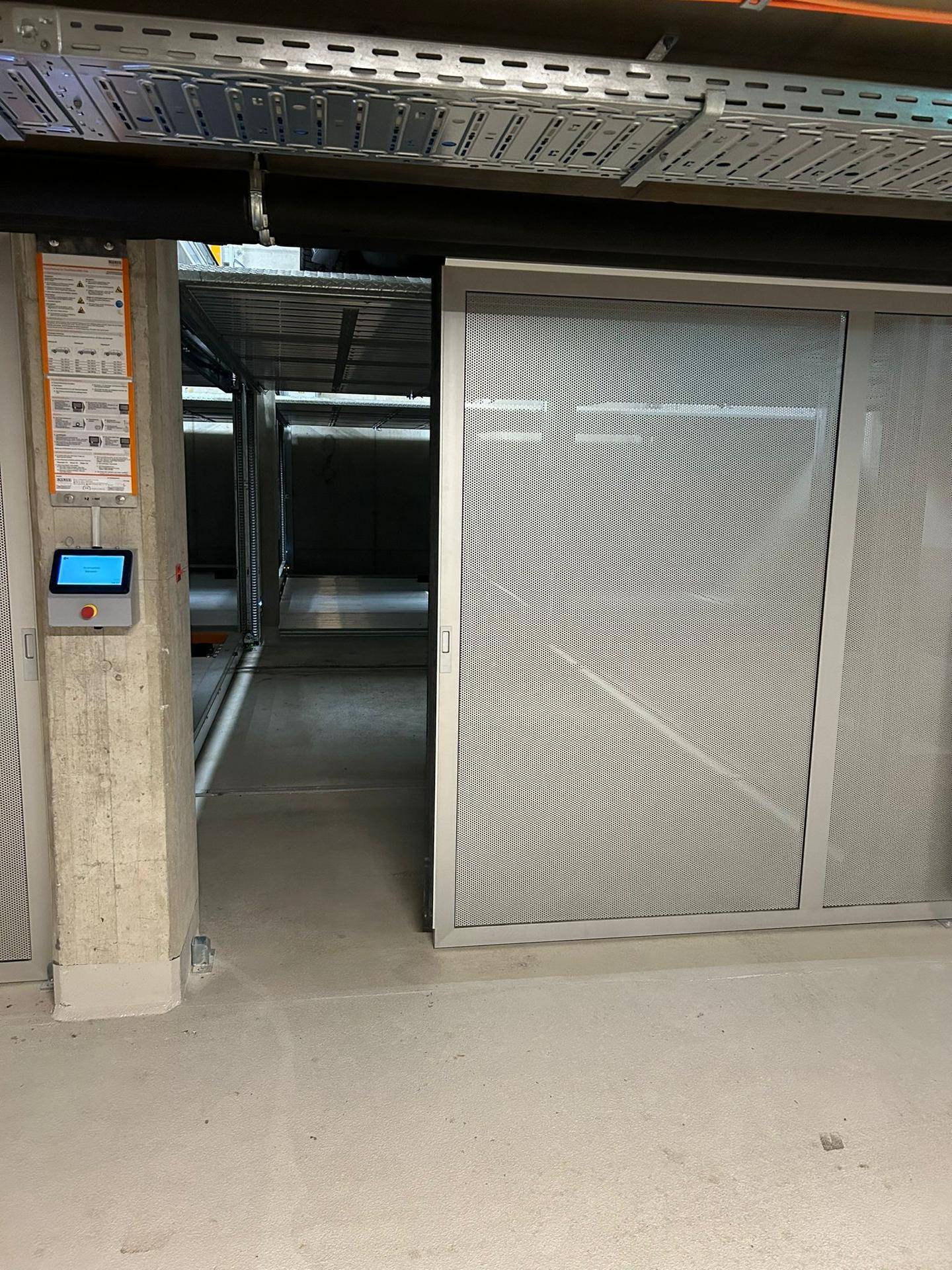 Eingang zu einer automatisierten Parkbucht in einer Tiefgarage mit Bedienfeld und Blick auf das Parksystem.