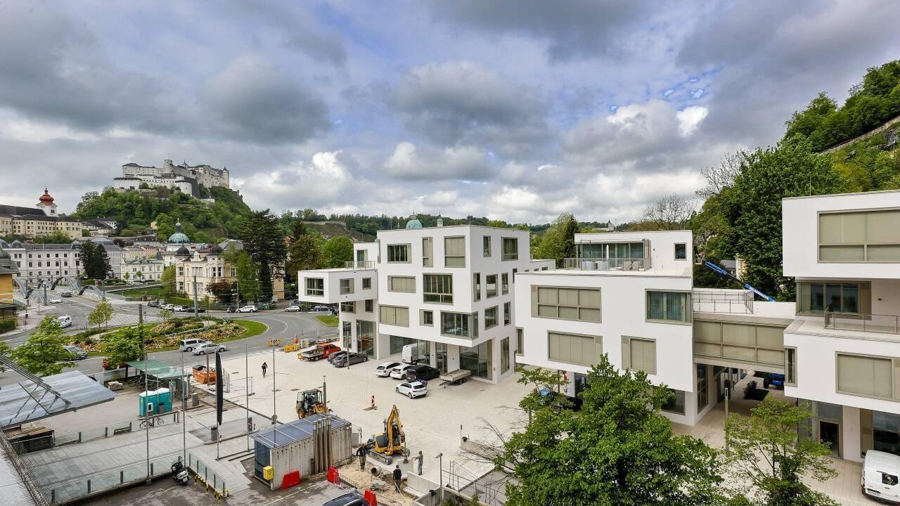 Weitläufige Ansicht eines modernen Gebäudekomplexes mit Baustelle und Blick auf die Stadt und Festung Hohensalzburg.