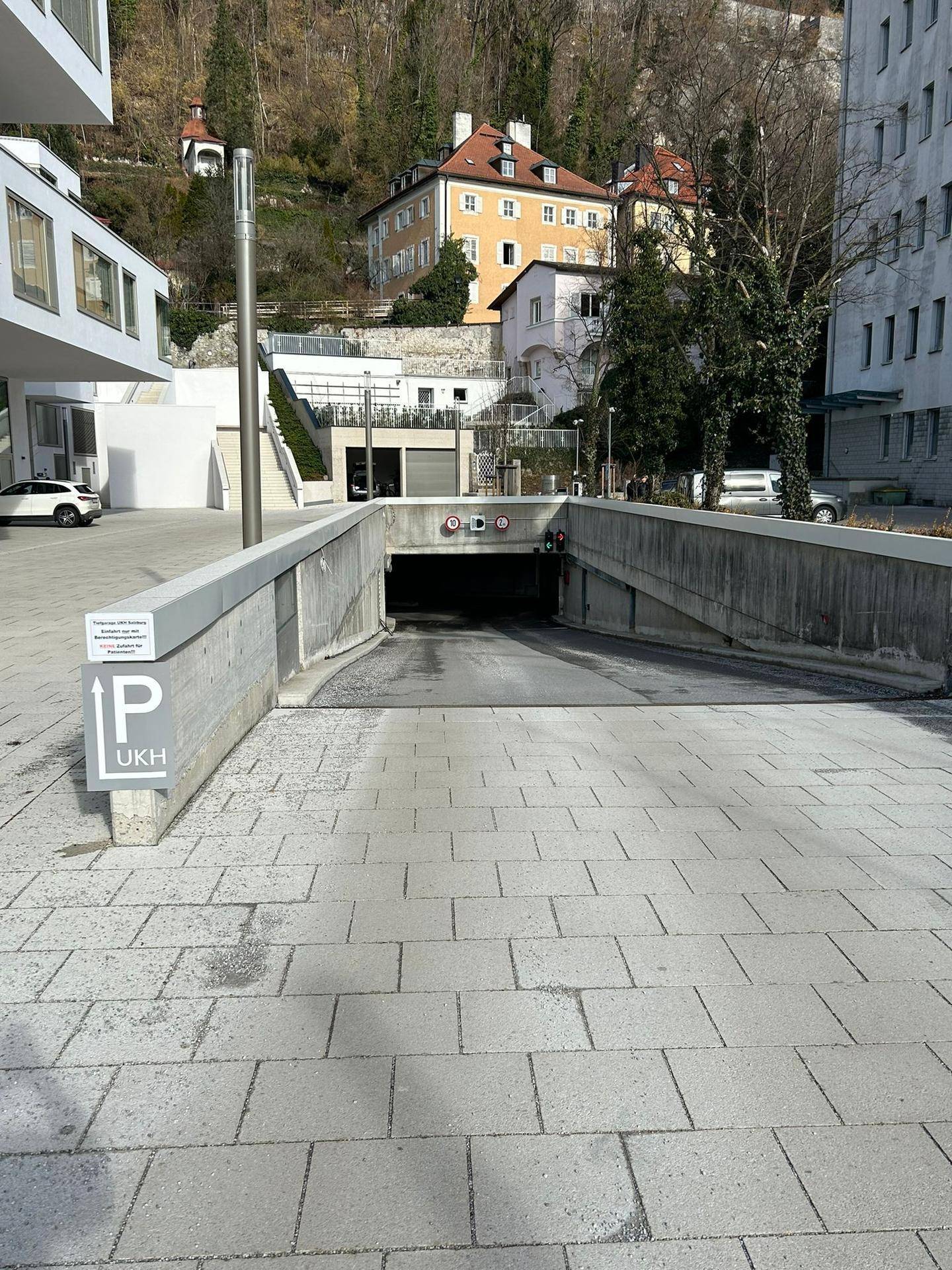 Eingang zu einer Tiefgarage mit Parkplatzschild und Gebäuden am Hang im Hintergrund.