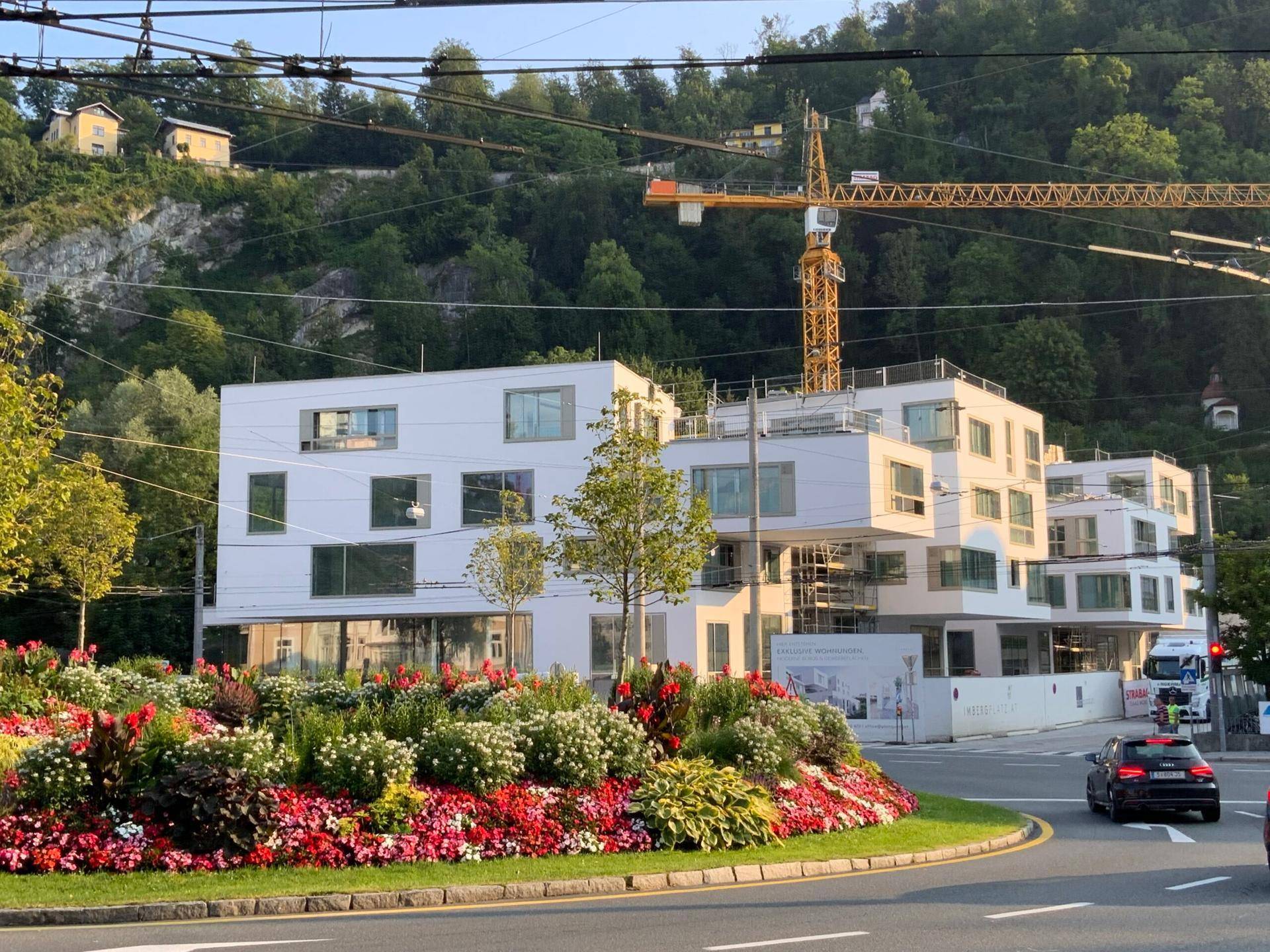Modernes Gebäude im Bau mit ansprechender Blumenbepflanzung im Vordergrund und einem Baukran im Hintergrund.