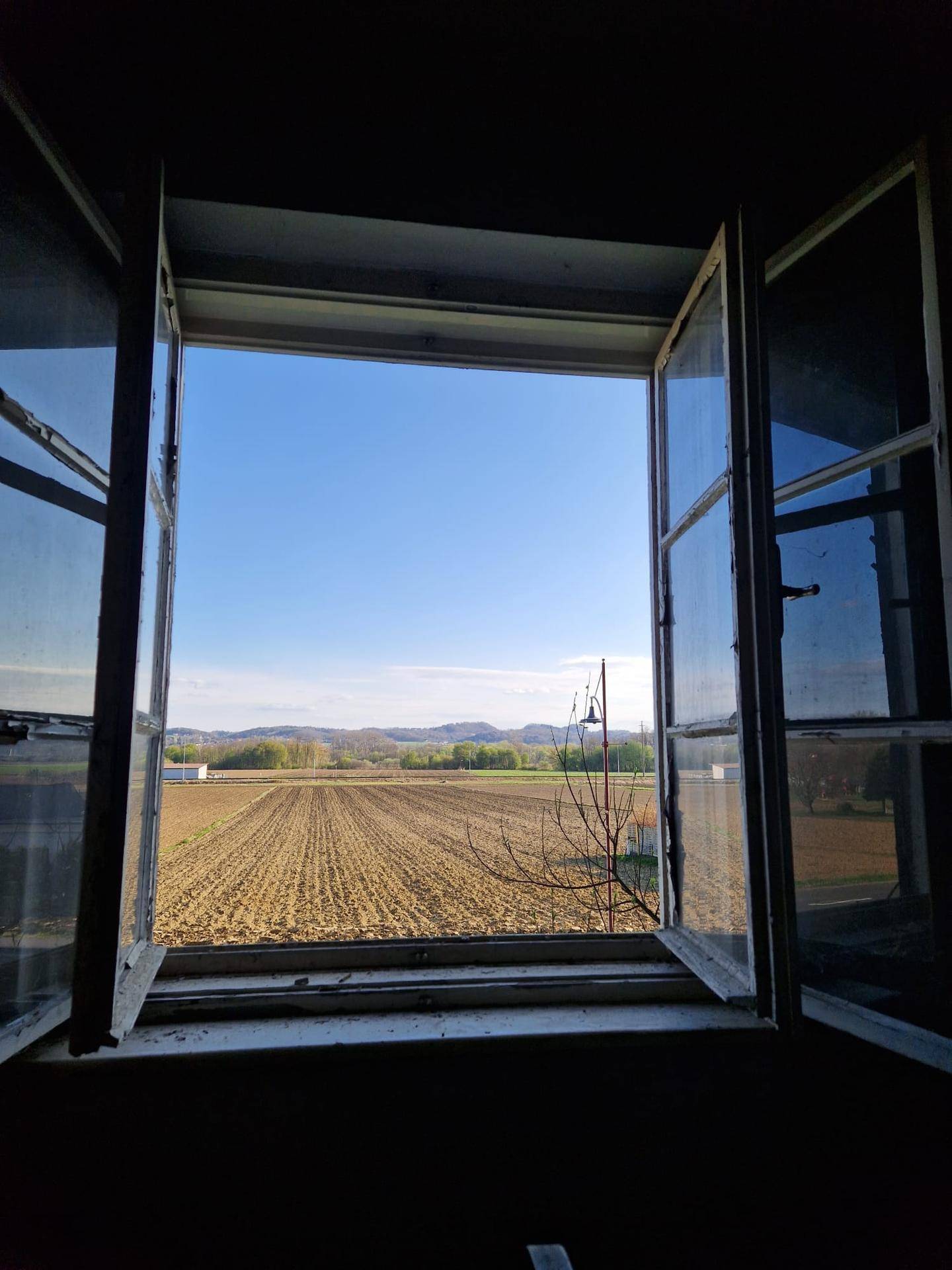 Fensterblick auf weite Felder und eine ländliche Landschaft unter blauem Himmel.