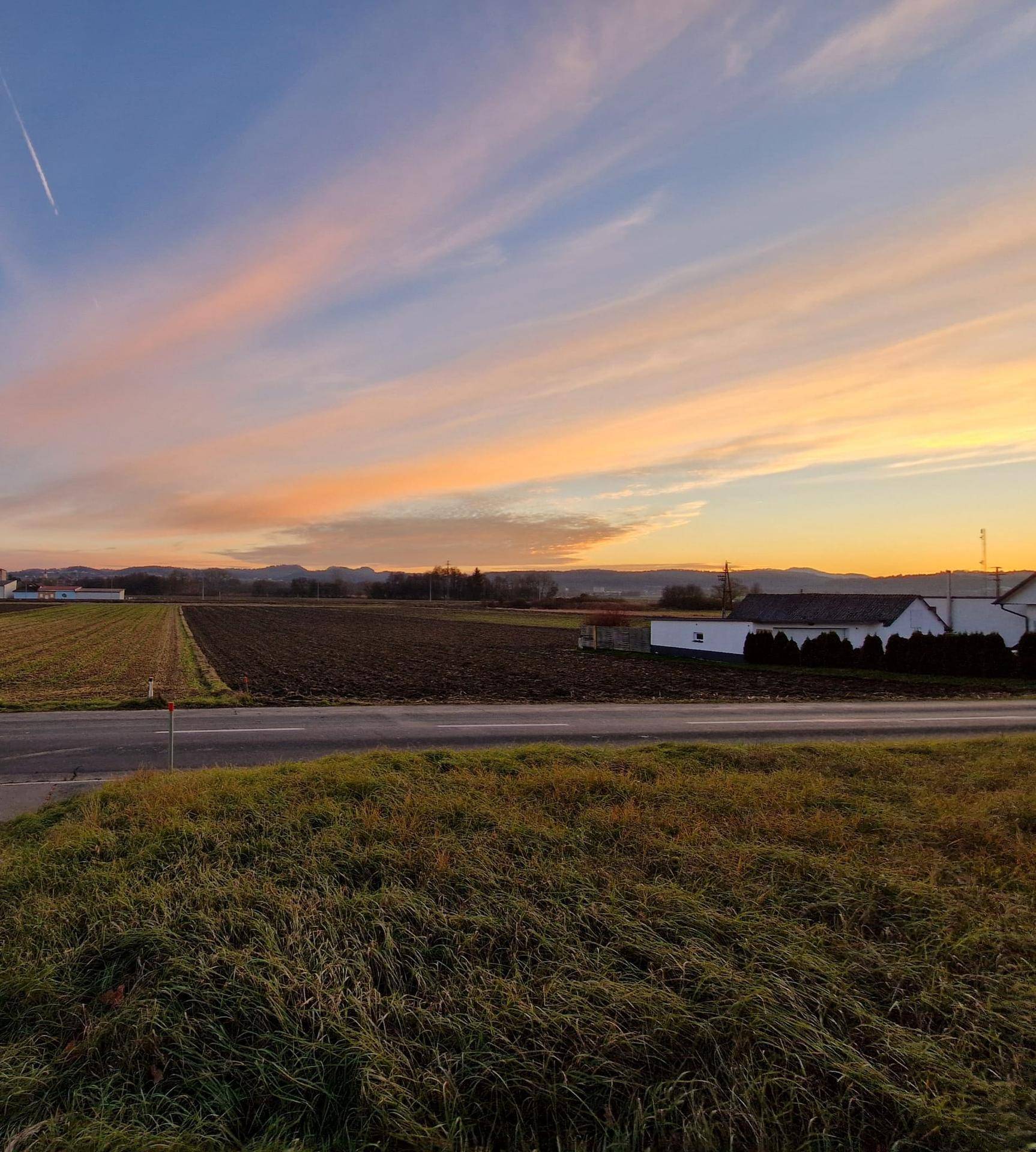 Malerischer Sonnenuntergang über weiten Feldern und einer Landstraße mit farbenfrohem Himmel.