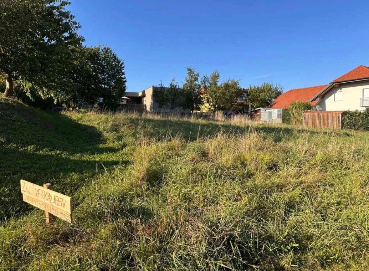 Grünes Baugrundstück mit 'Zu Verkaufen'-Schild in ländlicher Umgebung.
