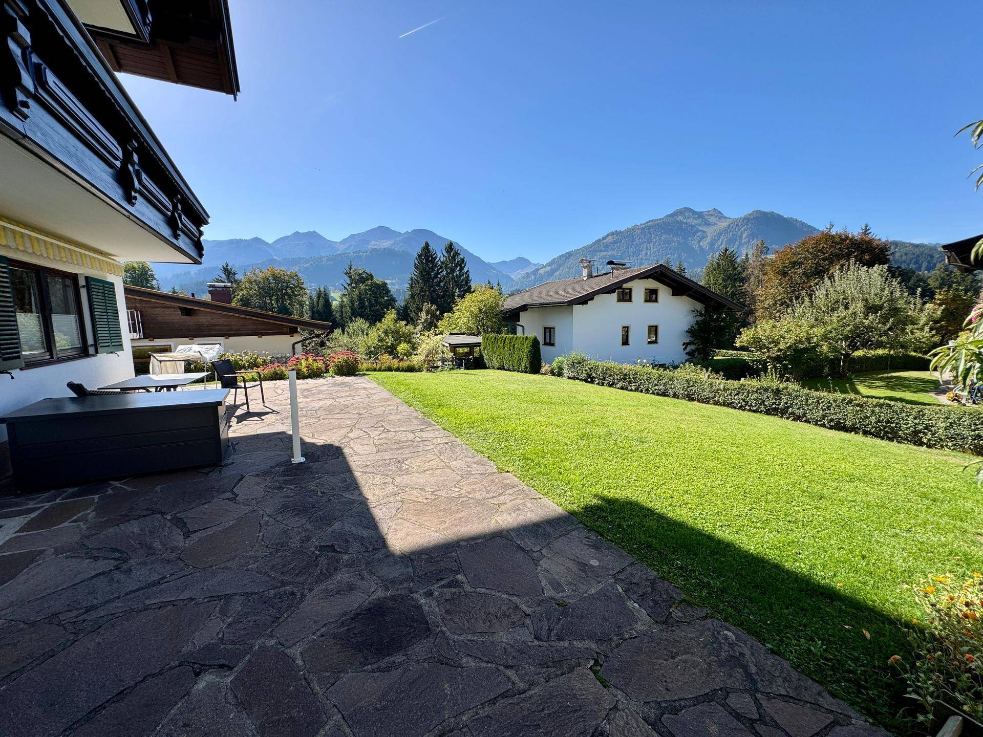 Großzügiger Gartenbereich mit Steinterrasse, Rasenfläche und beeindruckendem Bergblick.