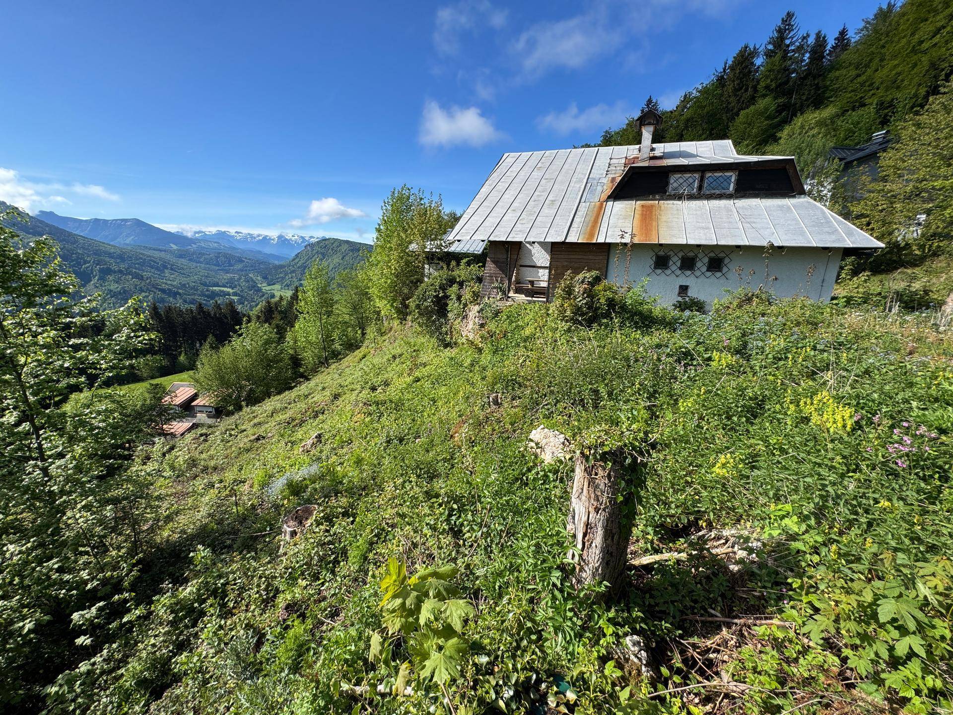 Rustikales Haus am Hang, umgeben von üppigem Grün mit Panoramablick auf die Berge.