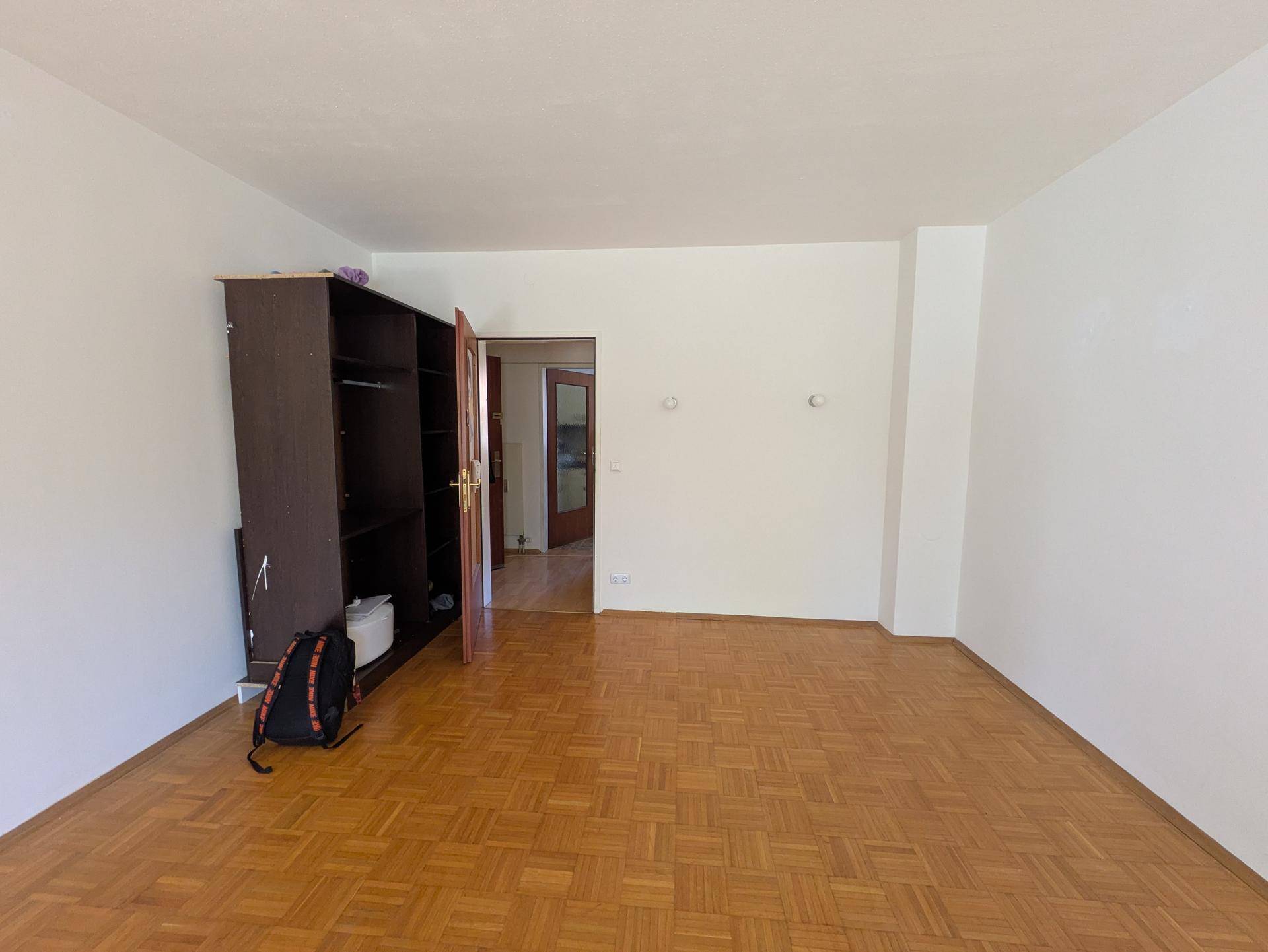 Geräumiger, leerer Raum mit Parkettboden und einem Kleiderschrank, der zu einem weiteren Bereich führt.