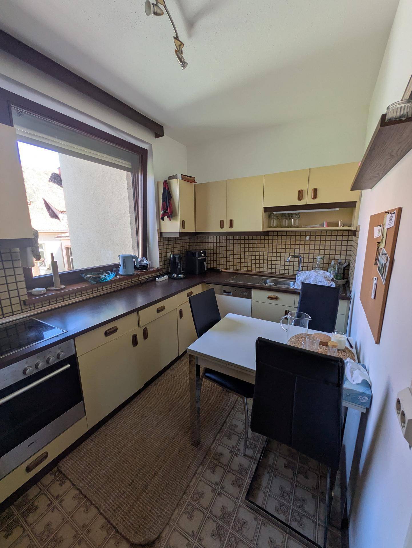 Funktionale Küche mit älteren Einbauschränken, Essbereich und einem Fenster für Tageslicht.