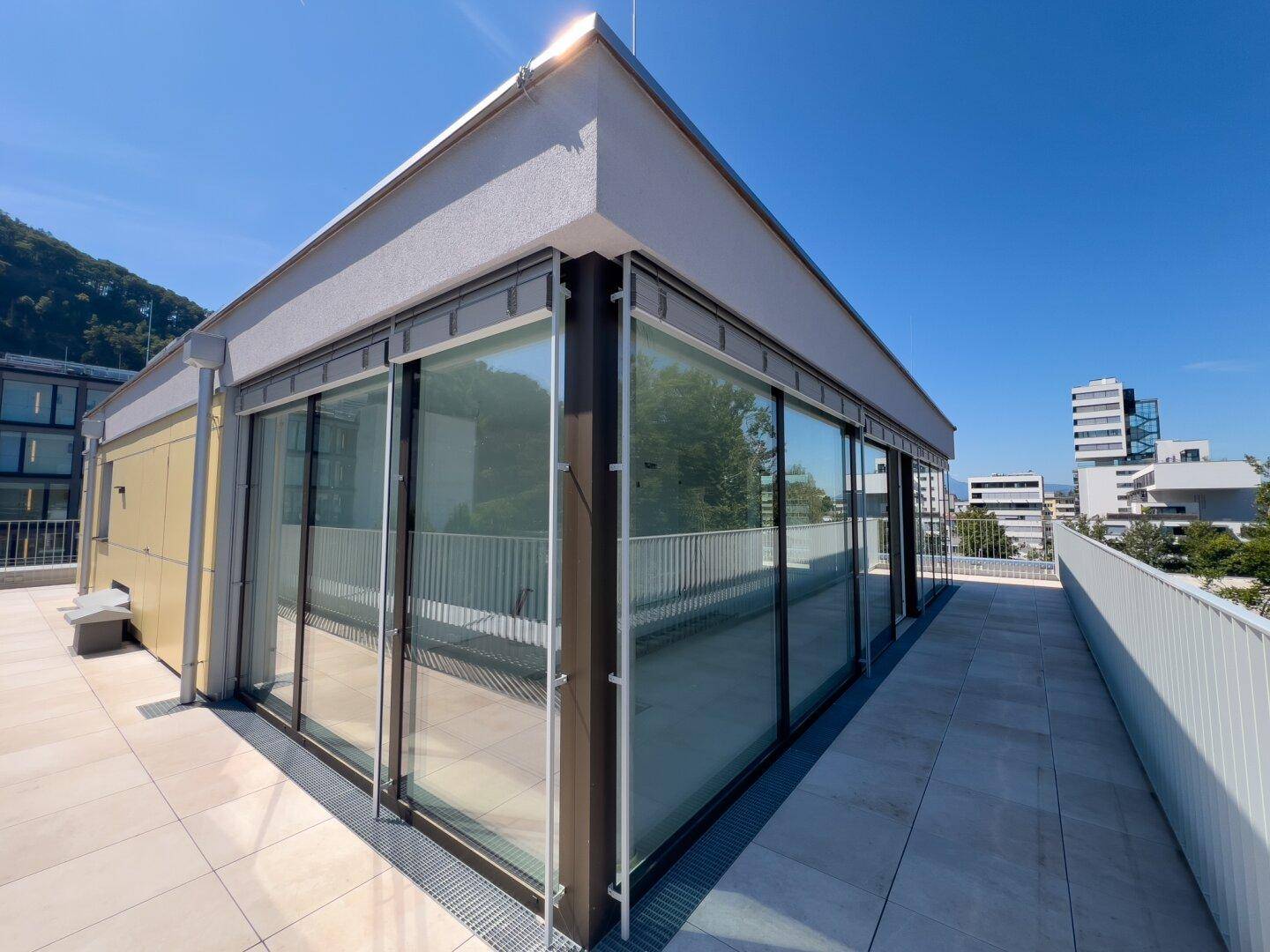 Moderne Architektur des Gebäudes mit großer Glasfassade und umlaufender Dachterrasse.