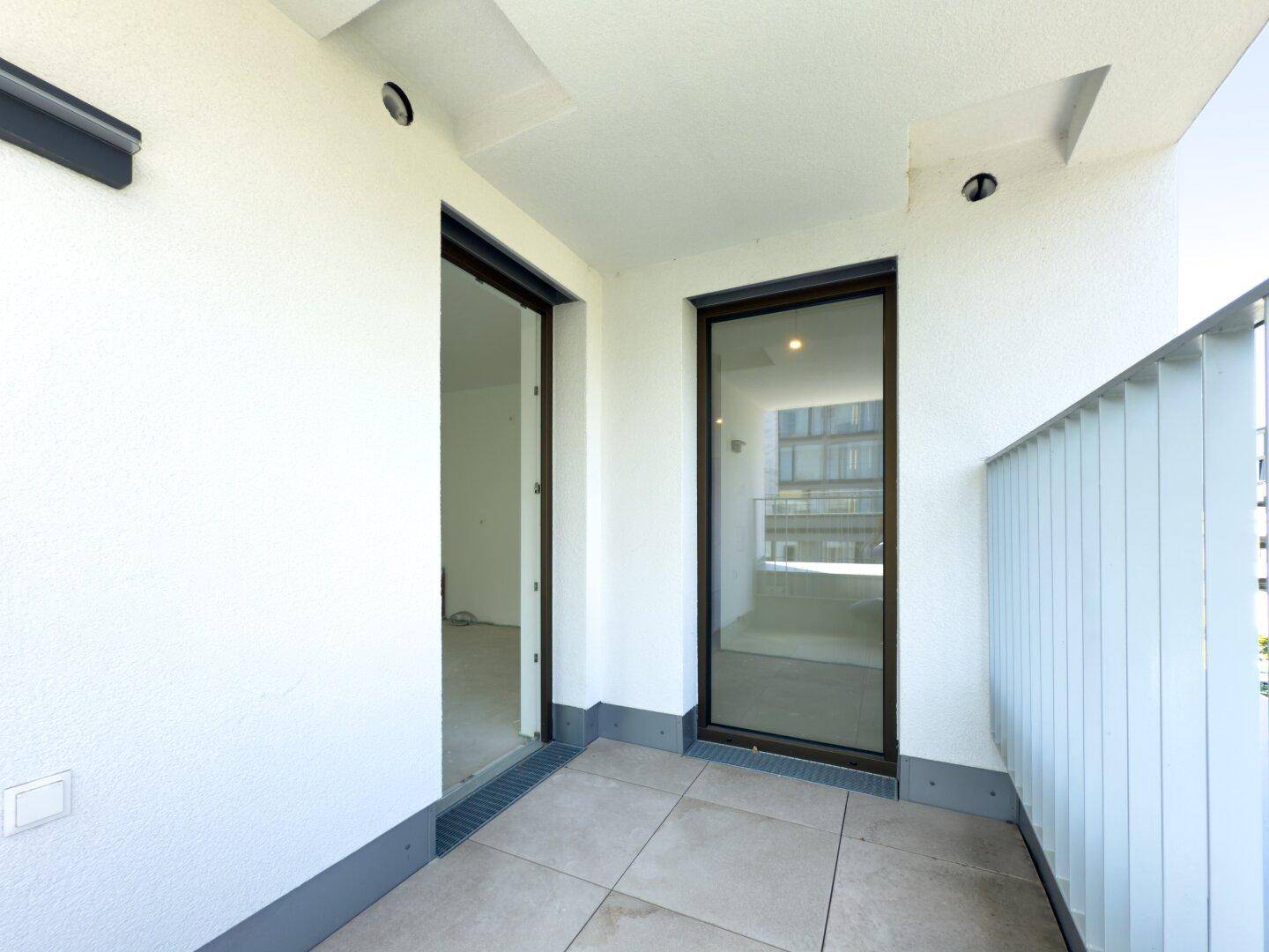 Heller Balkon mit Fliesenboden und moderner Brüstung, zugänglich von Innenräumen.