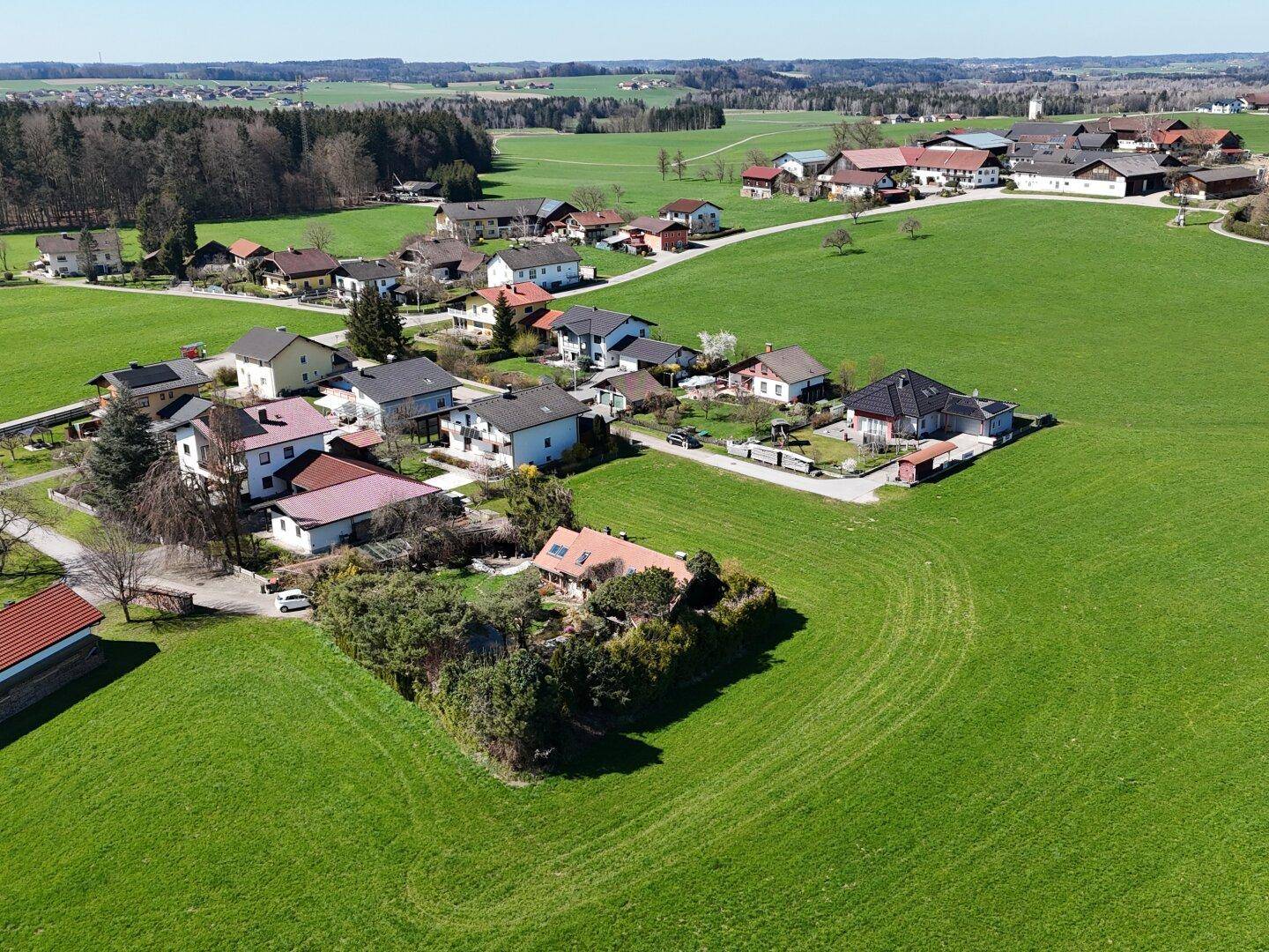 Weitläufige Luftaufnahme einer Wohnsiedlung eingebettet in grüne Wiesen und eine hügelige Landschaft.