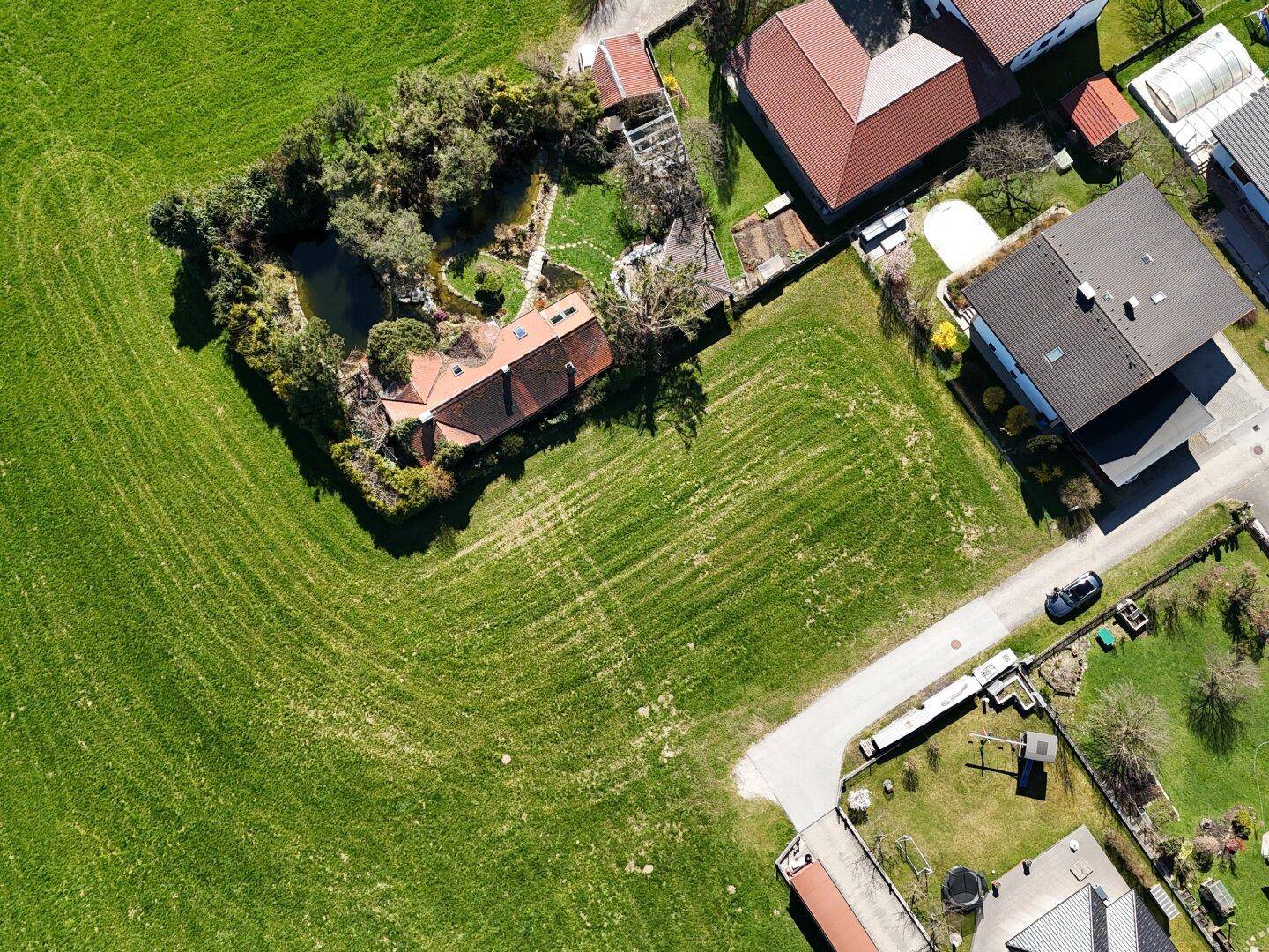Senkrechte Luftaufnahme eines Grundstücks mit angrenzenden Häusern und einem Teich in einem Garten.