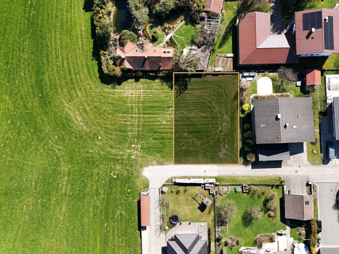 Senkrechte Luftaufnahme eines Baugrundstücks in ländlicher Umgebung mit angrenzenden Häusern.