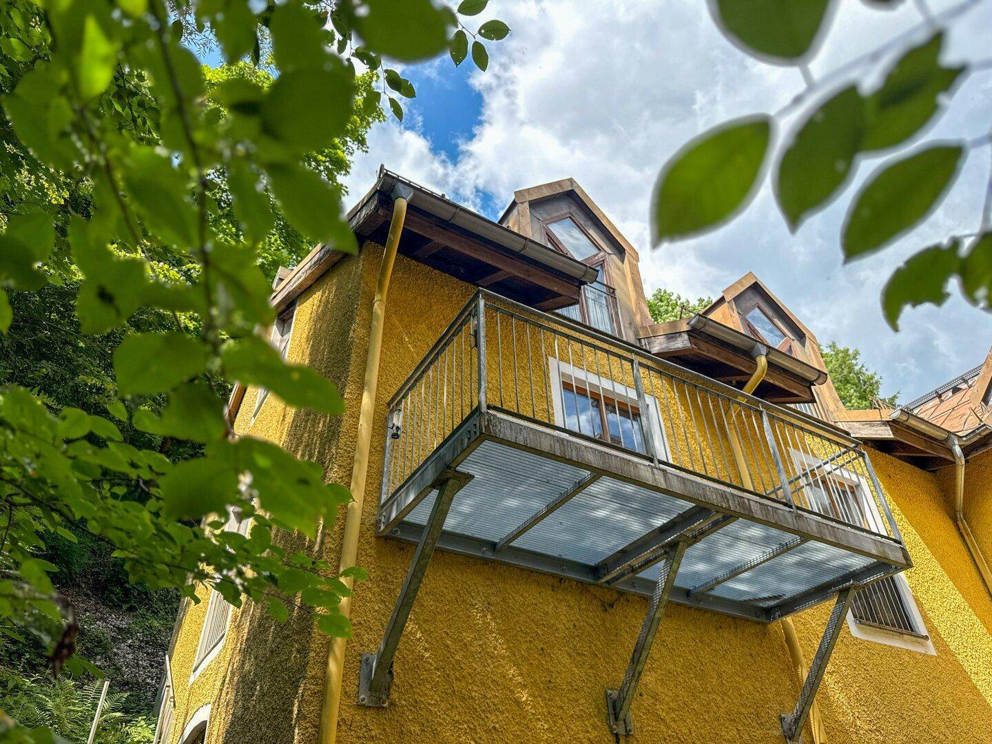 Gelbe Fassade eines Gebäudes mit mehreren Balkonen und Dachgauben, umgeben von Bäumen.
