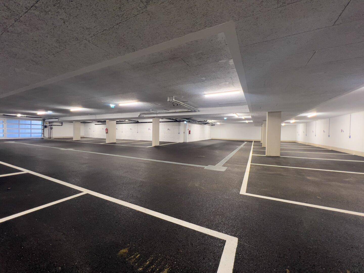 Große Tiefgarage mit zahlreichen markierten Stellplätzen und heller Beleuchtung.