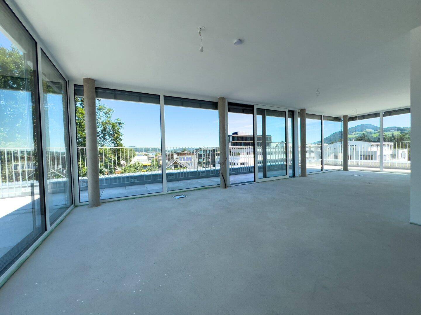Geräumiger, unmöblierter Innenraum mit großen Fensterfronten und weitem Ausblick auf die Umgebung.