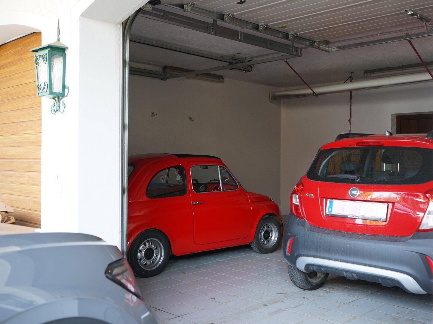 Geräumige Garage mit zwei geparkten Autos und einem geöffneten Garagentor.