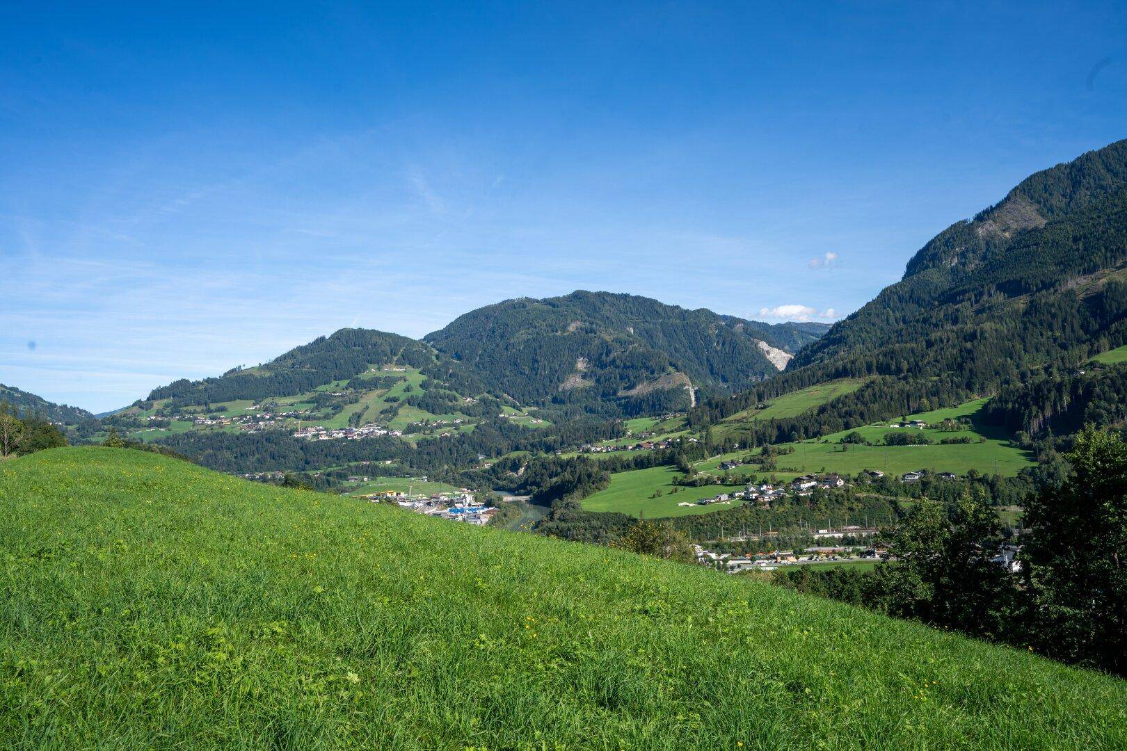 Weitläufiger Blick über grüne Hügel und Täler mit majestätischen Bergen im Hintergrund.
