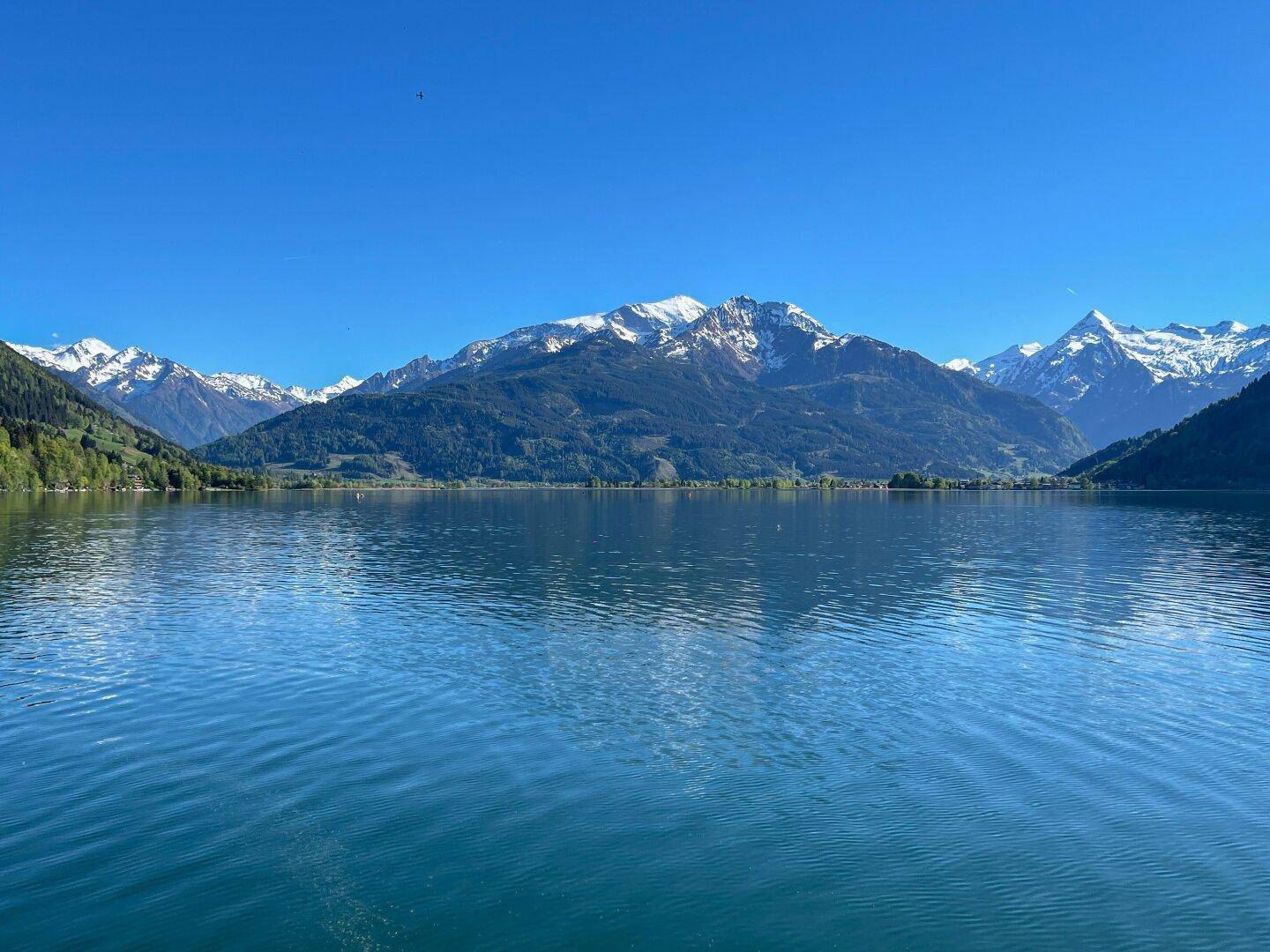 Malerischer See mit schneebedeckten Bergen im Hintergrund unter strahlend blauem Himmel.