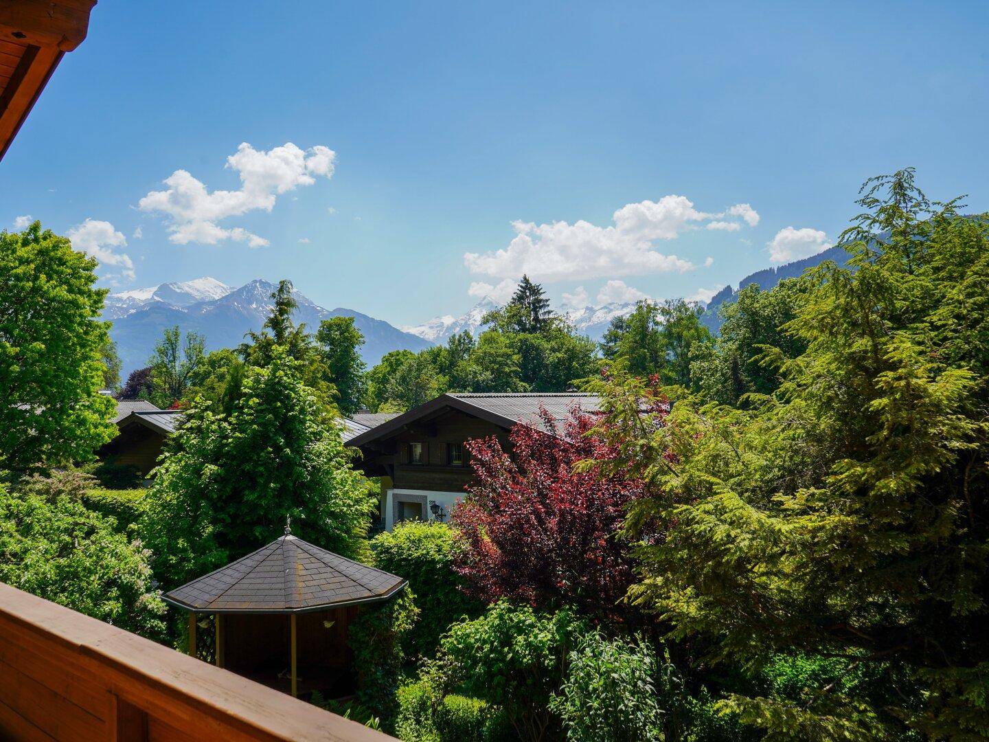 Panoramablick vom Balkon auf grüne Bäume, einen Pavillon und schneebedeckte Berge in der Ferne.