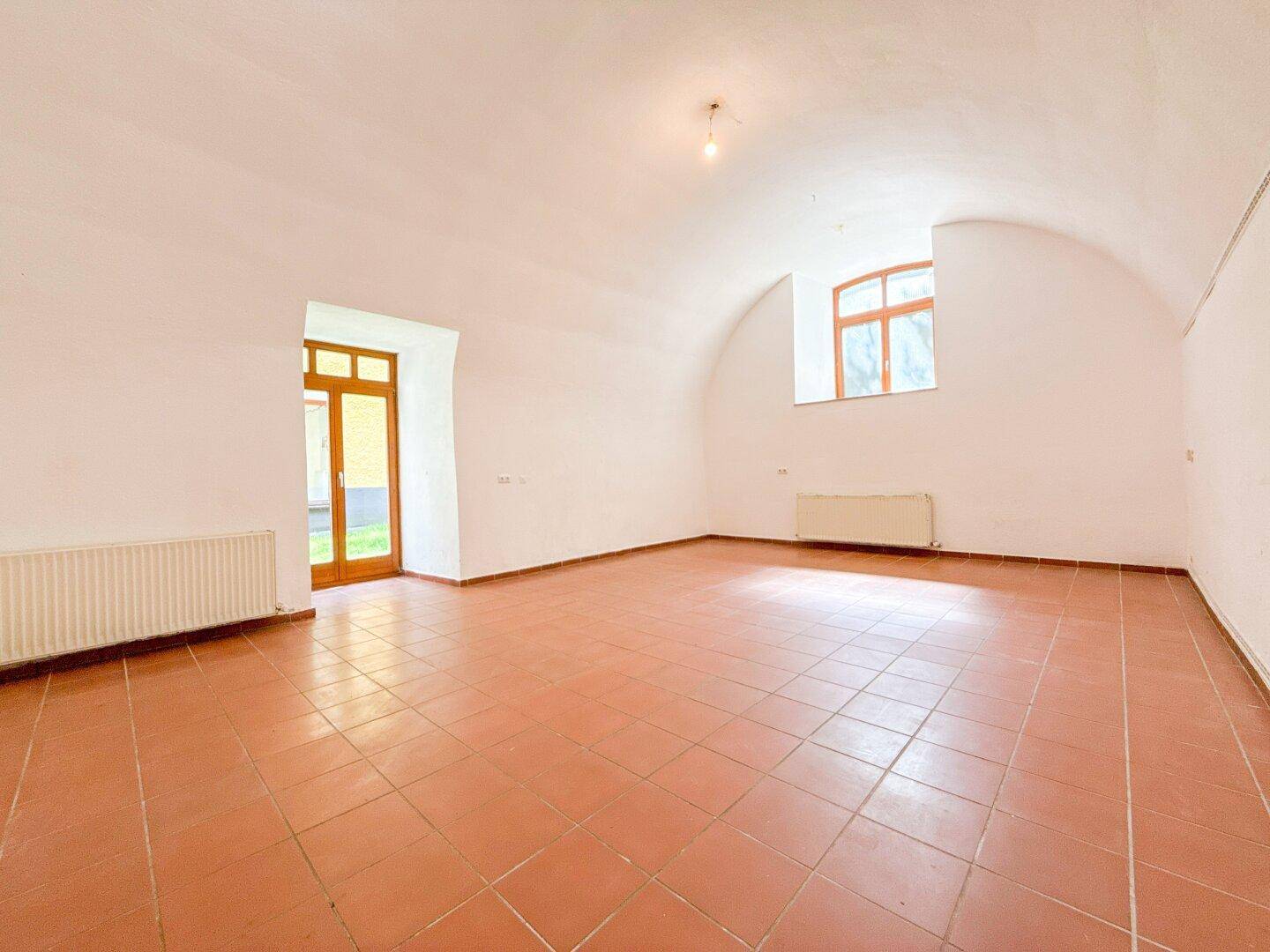 Geräumiger, leerer Raum mit Terrakottafliesen, Gewölbedecke und Zugang zum Außenbereich.