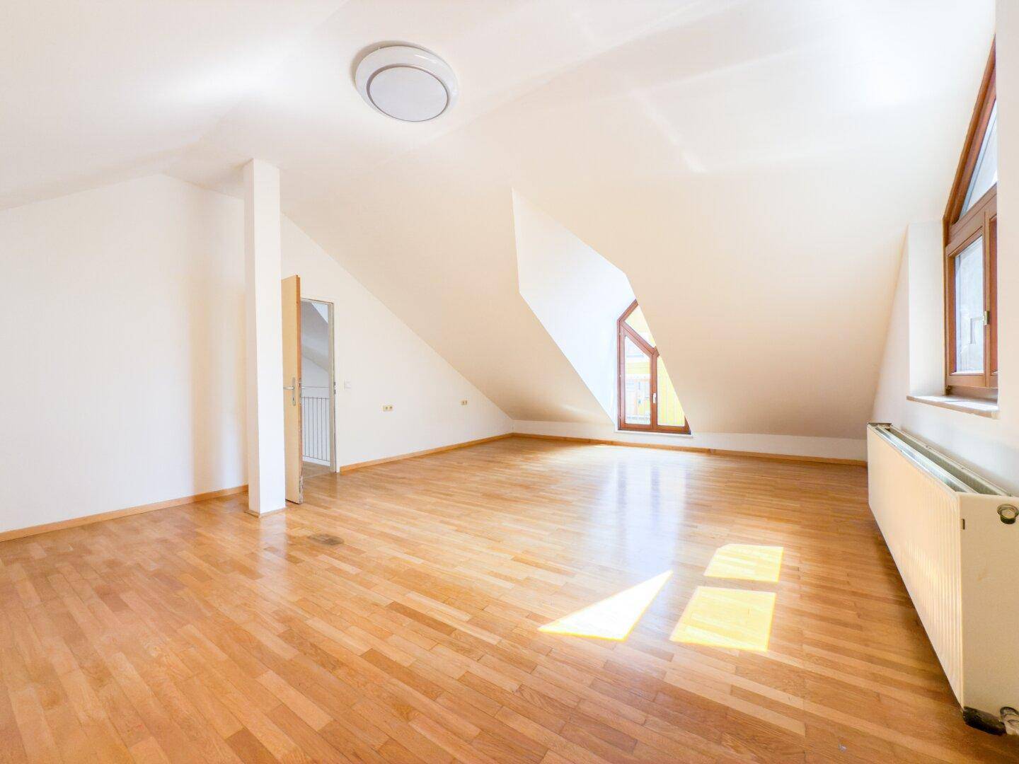 Helles Dachzimmer mit Holzboden und schrägen Wänden, bietet vielseitige Nutzungsmöglichkeiten.