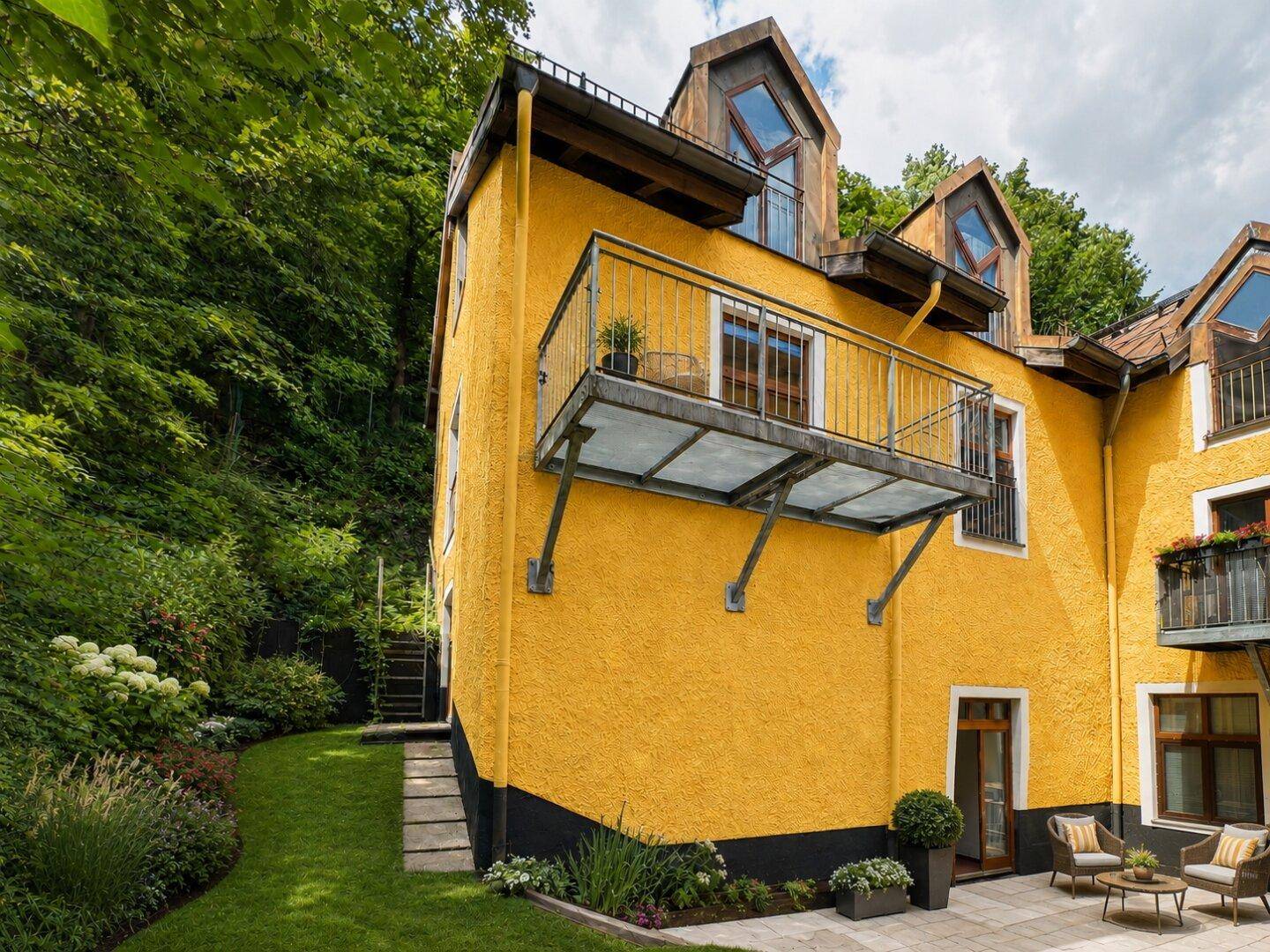 Gelbes Gebäude mit Terrasse, Garten und Balkonen, eingebettet in eine grüne Umgebung.