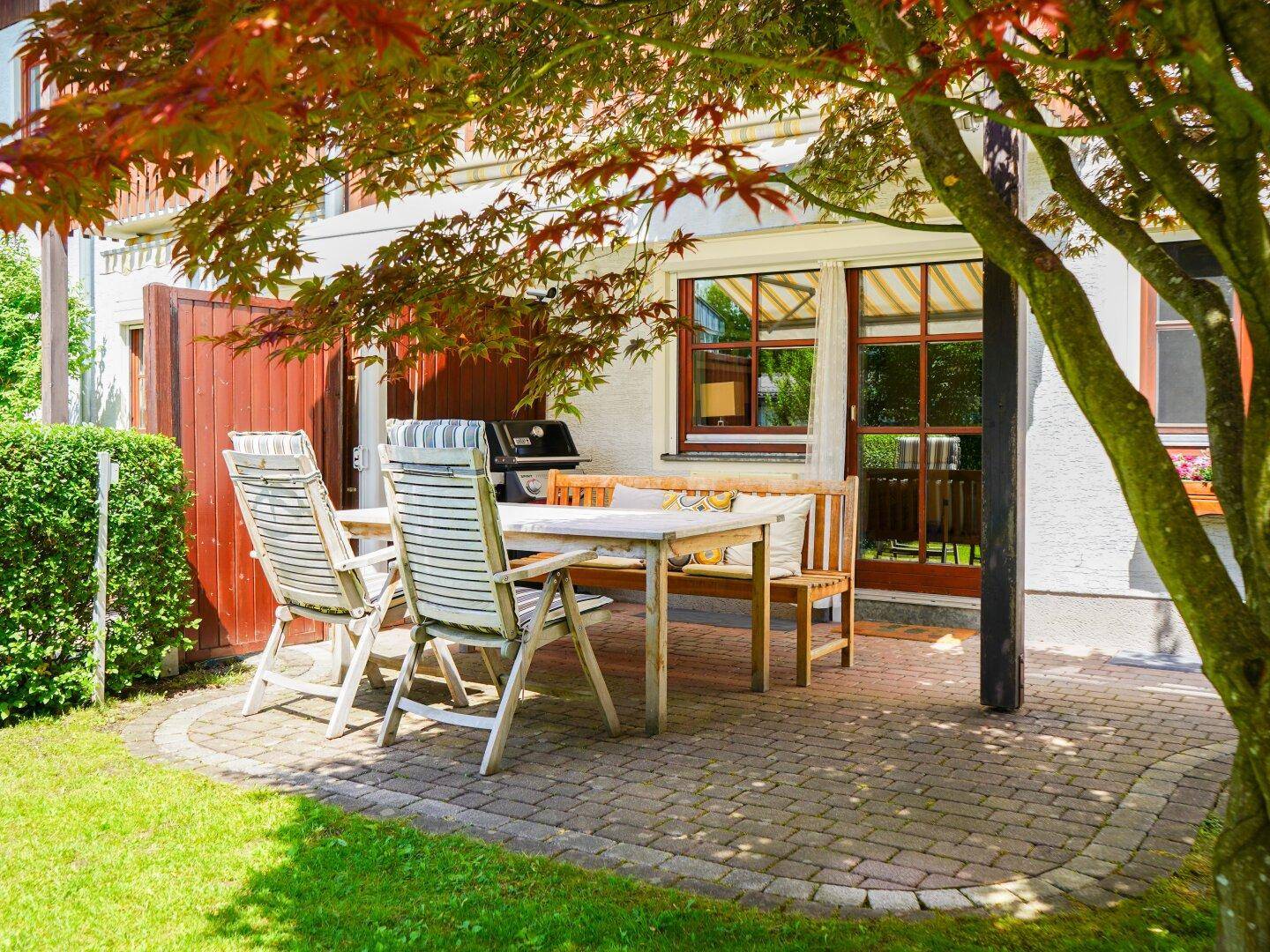 Sonnige Terrasse mit Esstisch, Grill und bequemen Stühlen, ideal für Mahlzeiten im Freien.