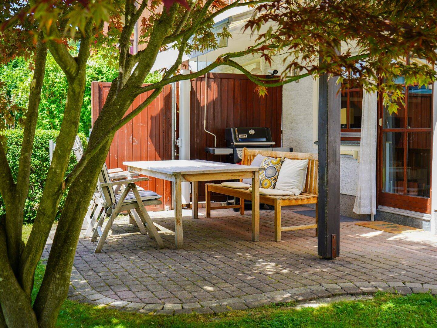 Gemütliche Terrasse mit Holztisch und Grill, ideal für entspannte Stunden im Freien unter dem Baum.