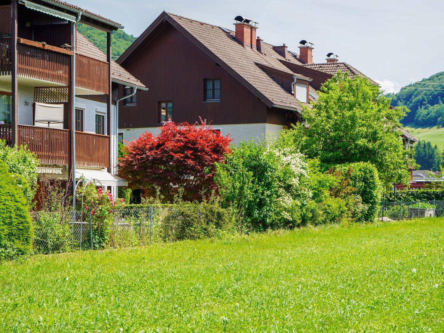 Wohngebäude mit Balkonen, eingebettet in eine grüne Landschaft mit weiten Feldern und Bergen im Hintergrund.
