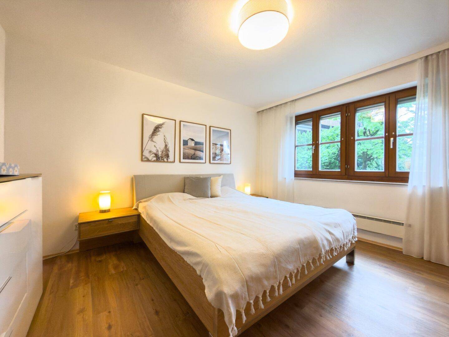 Ruhiges Schlafzimmer mit Doppelbett, Holzboden und großem Fenster, das viel Tageslicht hereinlässt.