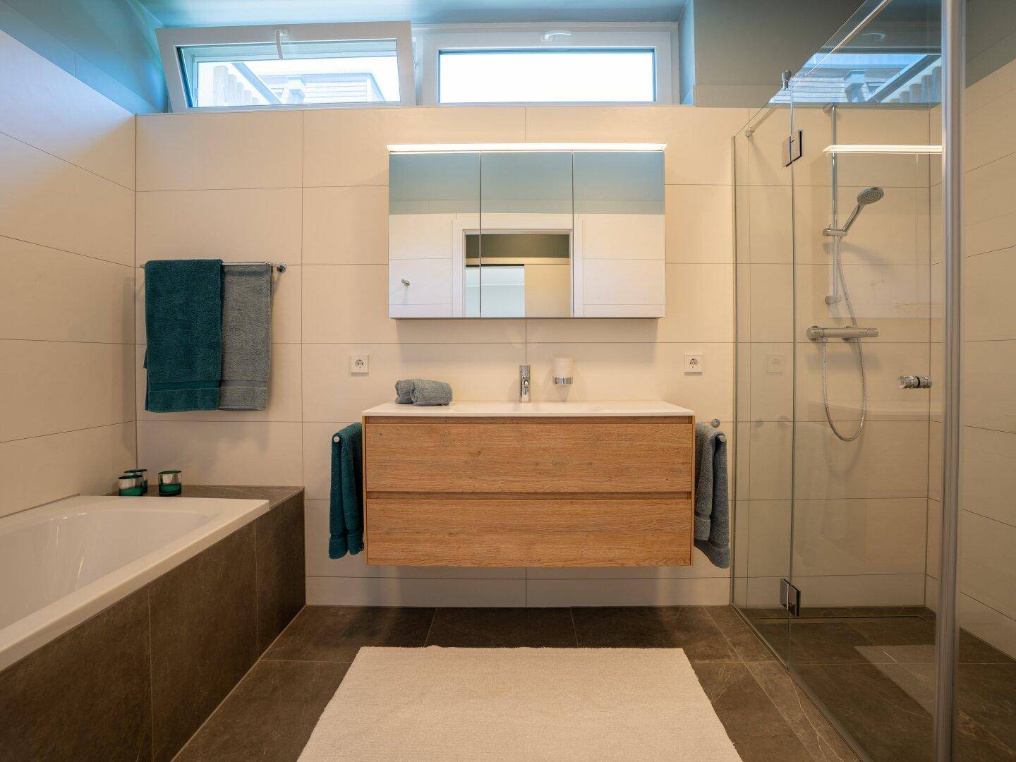 Modernes Badezimmer mit schwebendem Waschtisch, Badewanne, Dusche und Oberlichtern für Tageslicht.