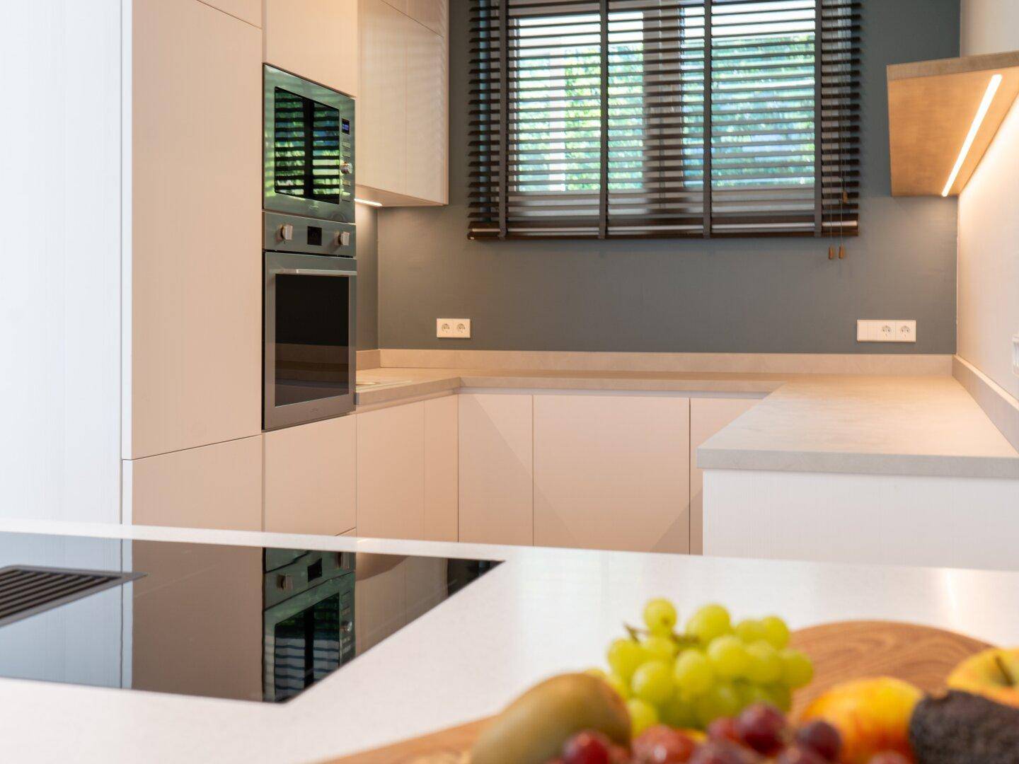 Moderne Küche mit weißen Schränken, integrierten Geräten und Fenster mit Jalousien.