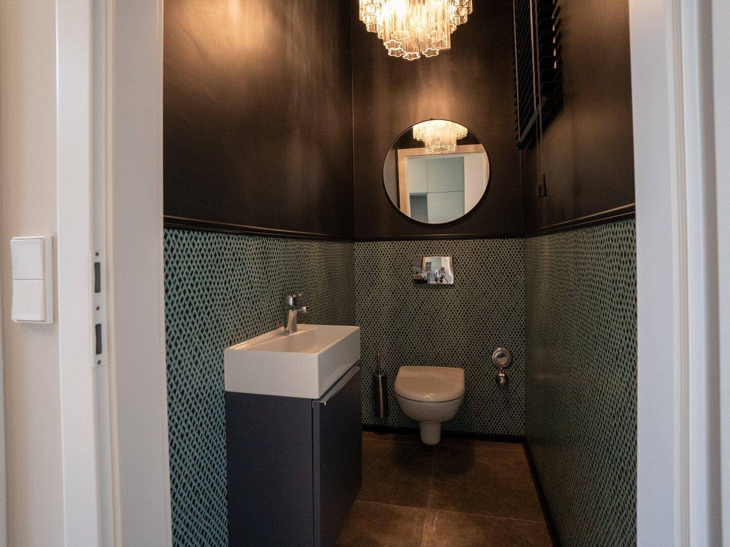 Stilvolles Gäste-WC mit dunklen Wänden, gemusterter Tapete und modernem Waschtisch mit Spiegel.