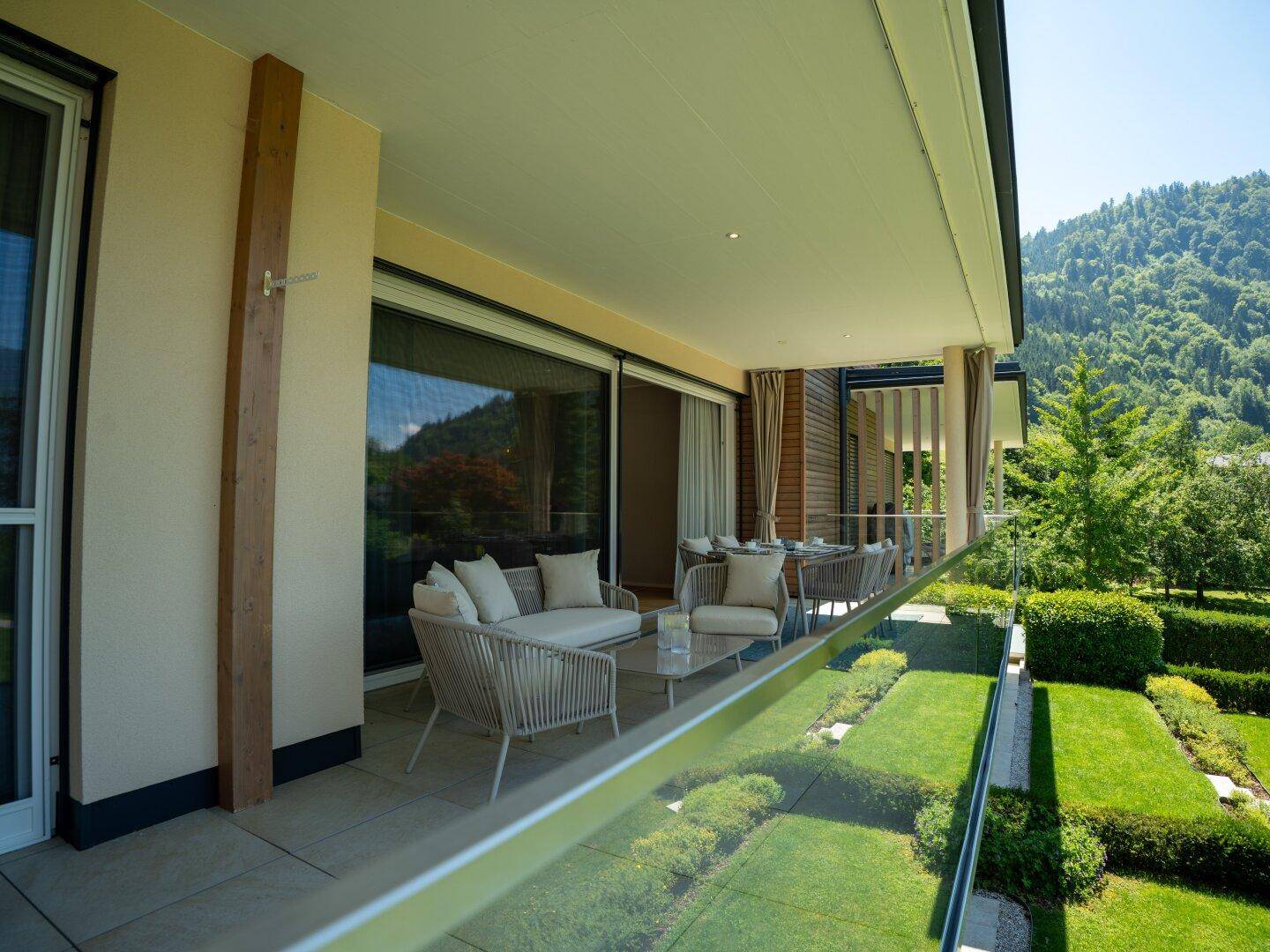 Langer Balkon mit Sitzgelegenheiten und Glasgeländer, bietet einen schönen Blick auf den gepflegten Garten.