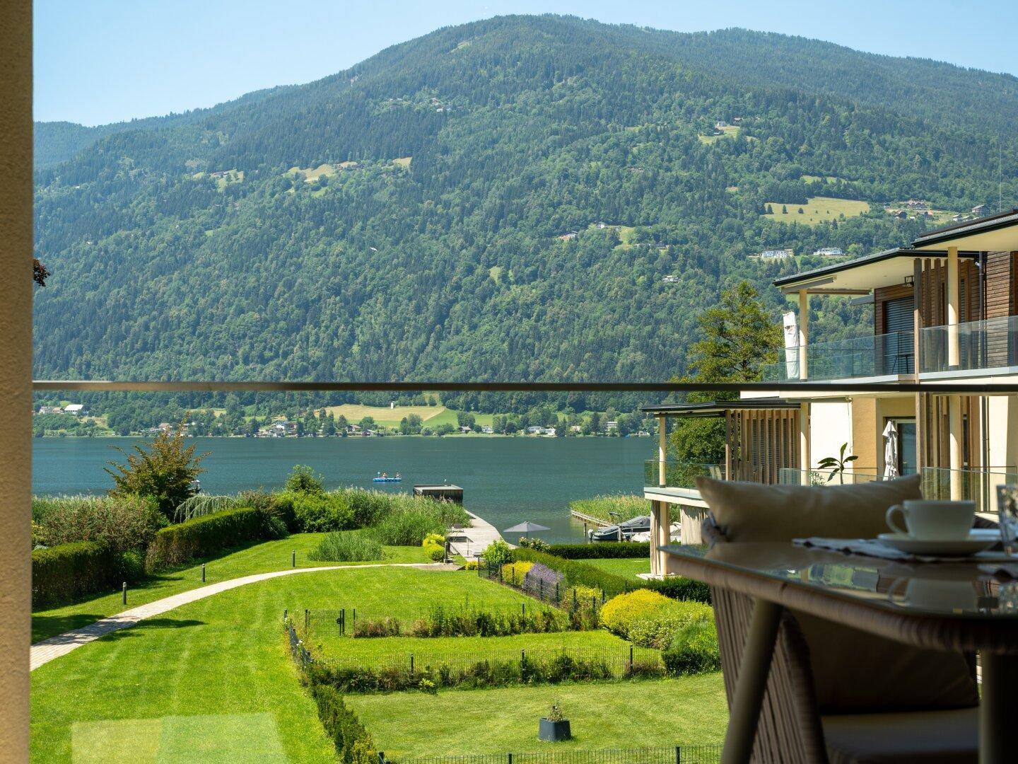 Weitläufiger Blick über den gepflegten Garten zum See und den majestätischen Bergen im Hintergrund.