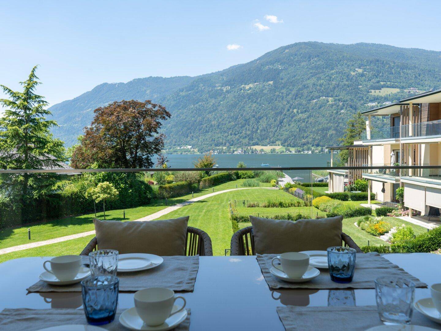 Sonniger Essbereich auf der Terrasse mit gedecktem Tisch, bietet einen weiten Blick auf den See und die Berge.